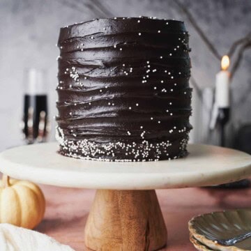 Black velvet cake on a cake plate with a pumpkin in the foreground and a candlestick and glass in the background.