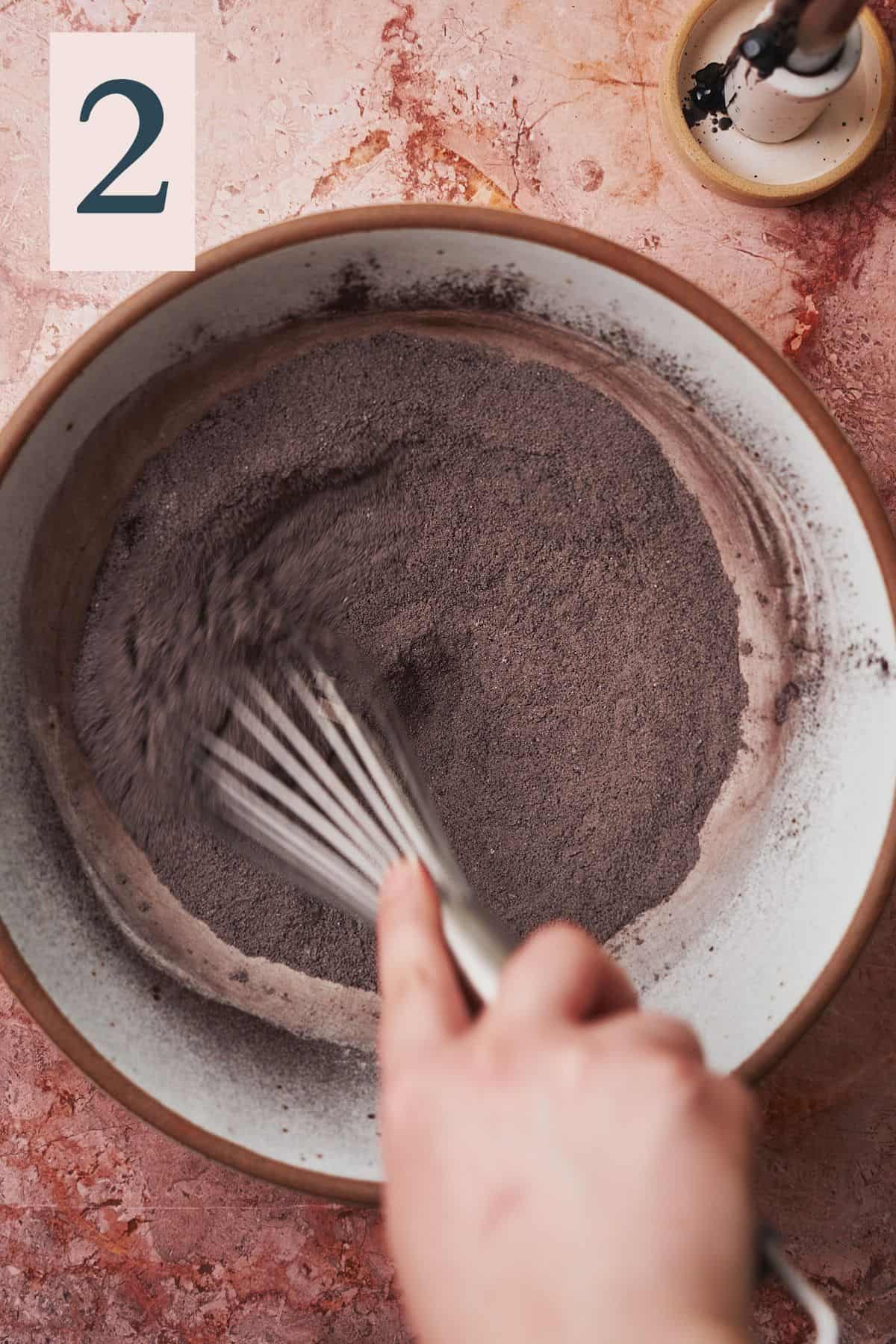 hand whisking black cocoa powder and other dry ingredients in a large bowl. 