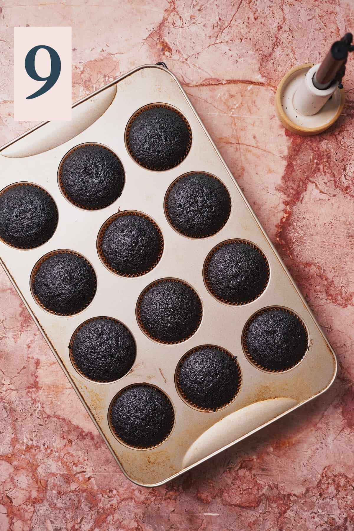 12 dark black cupcakes baked in a tin. 