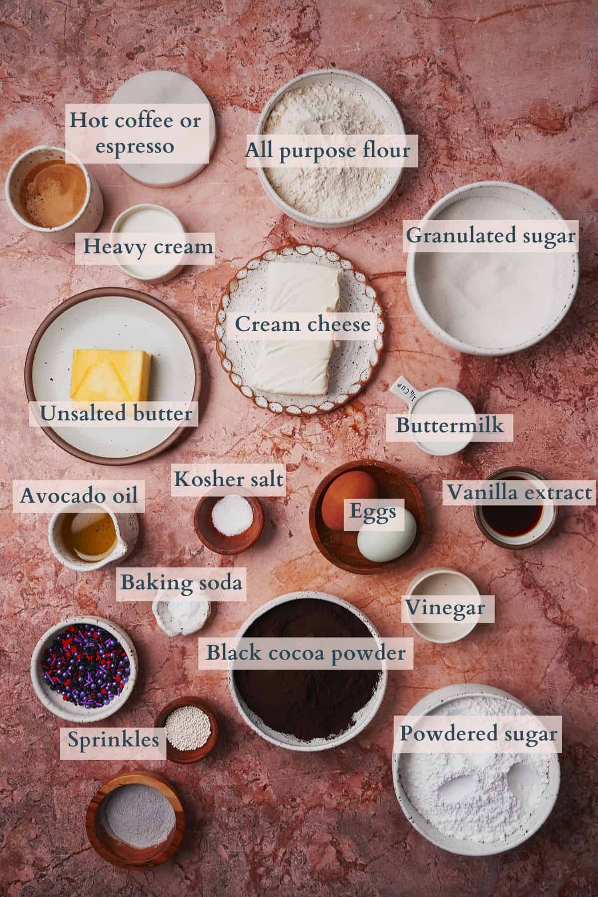 Ingredients to make black velvet cupcakes laid out on a table with text overlaying to denote each ingredient. 