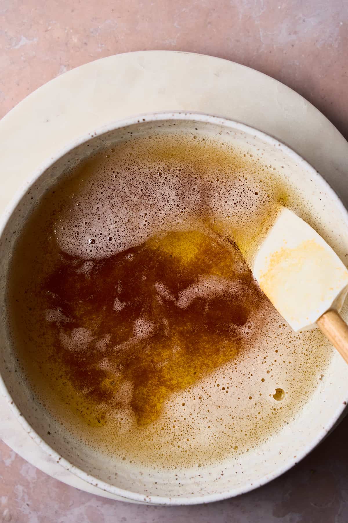 Brown butter in a bowl with a rubber spatula, to the side, showing the brown flecks on the bottom of the bowl. 