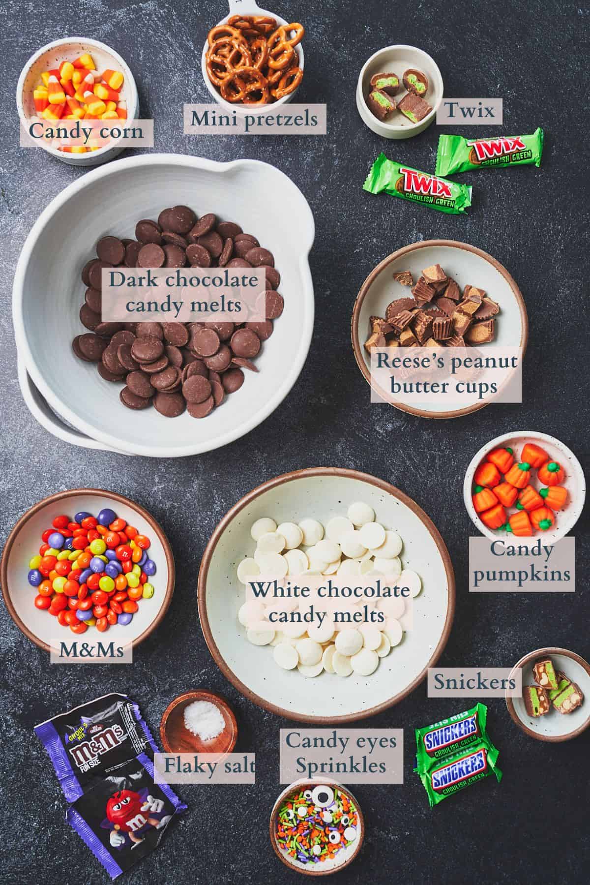 Ingredients to make Halloween bark laid out on a table in small bowls with text overlaying to denote each ingredient. 