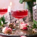 Beautiful love potion cocktail with dry ice falling out, surrounded by roses, with a candlestick burning in the background.