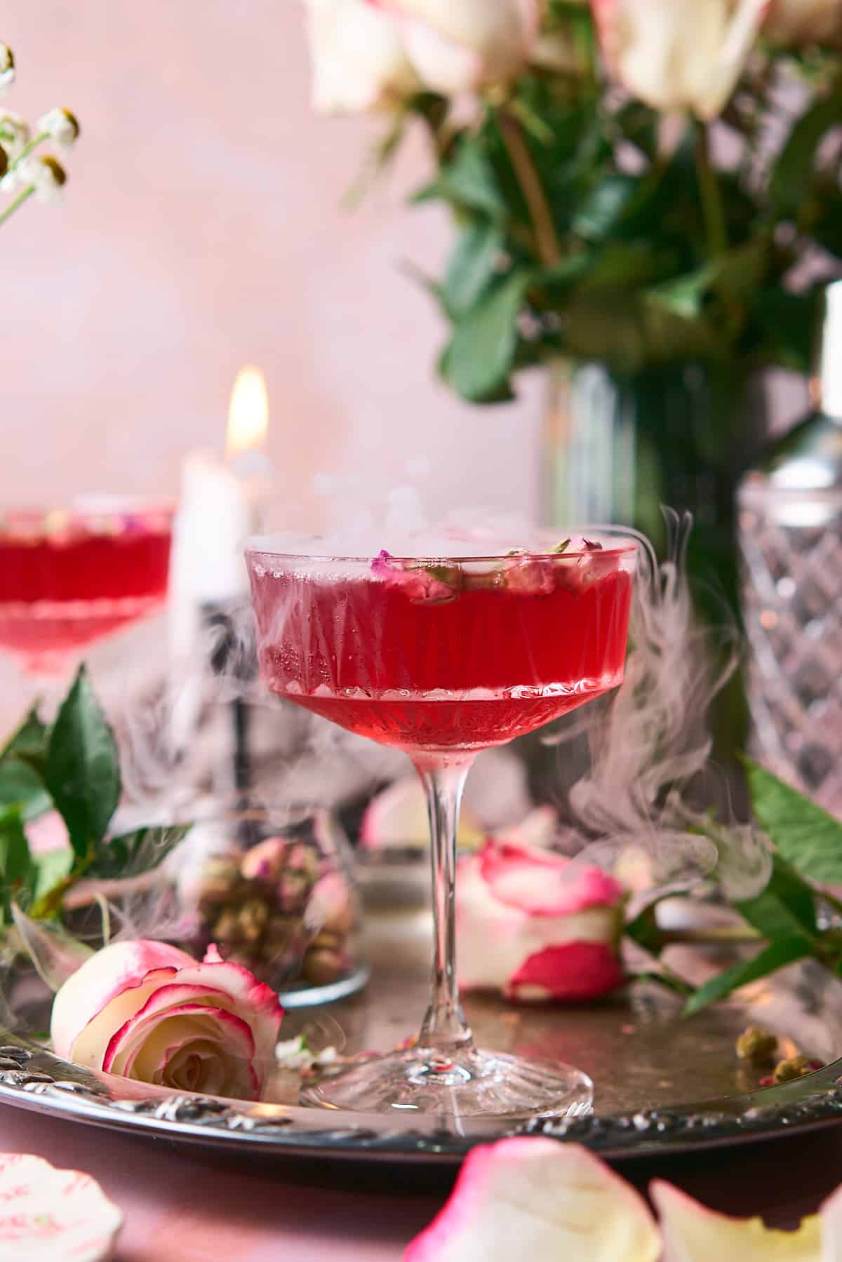 stunning scene of a bright pink love potion cocktail, with roses around it, and dry ice coming out of the cocktail. 