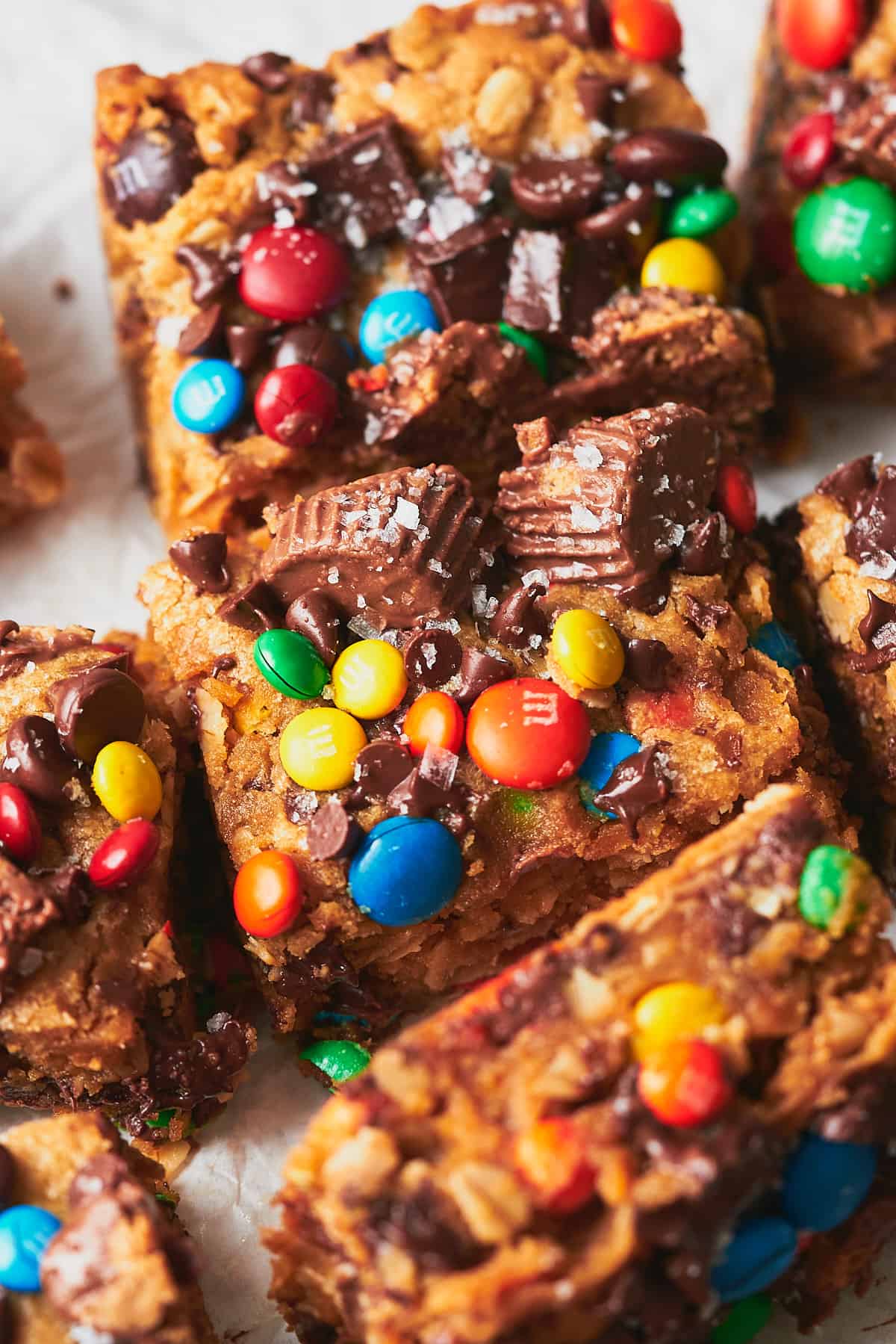 close up shot of monster cookie bars with candy and flakey sea salt cut into pieces on white parchment paper. 