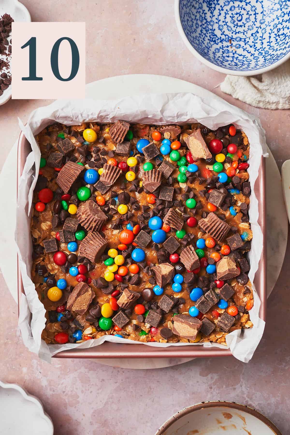 cookie dough pressed into a square baking pan and topped with reese's, M&ms, chocolate chips, and chunks. 