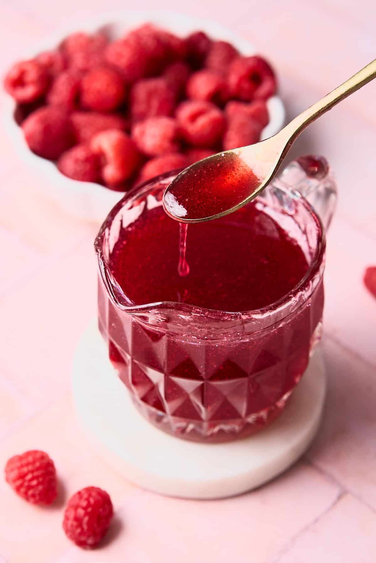 Delicious red raspberry syrup in a decorative glass being held by a spoon.