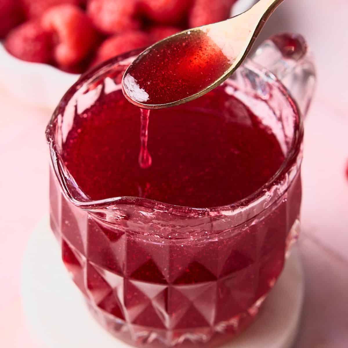 Delicious raspberry syrup held on a golden spoon.