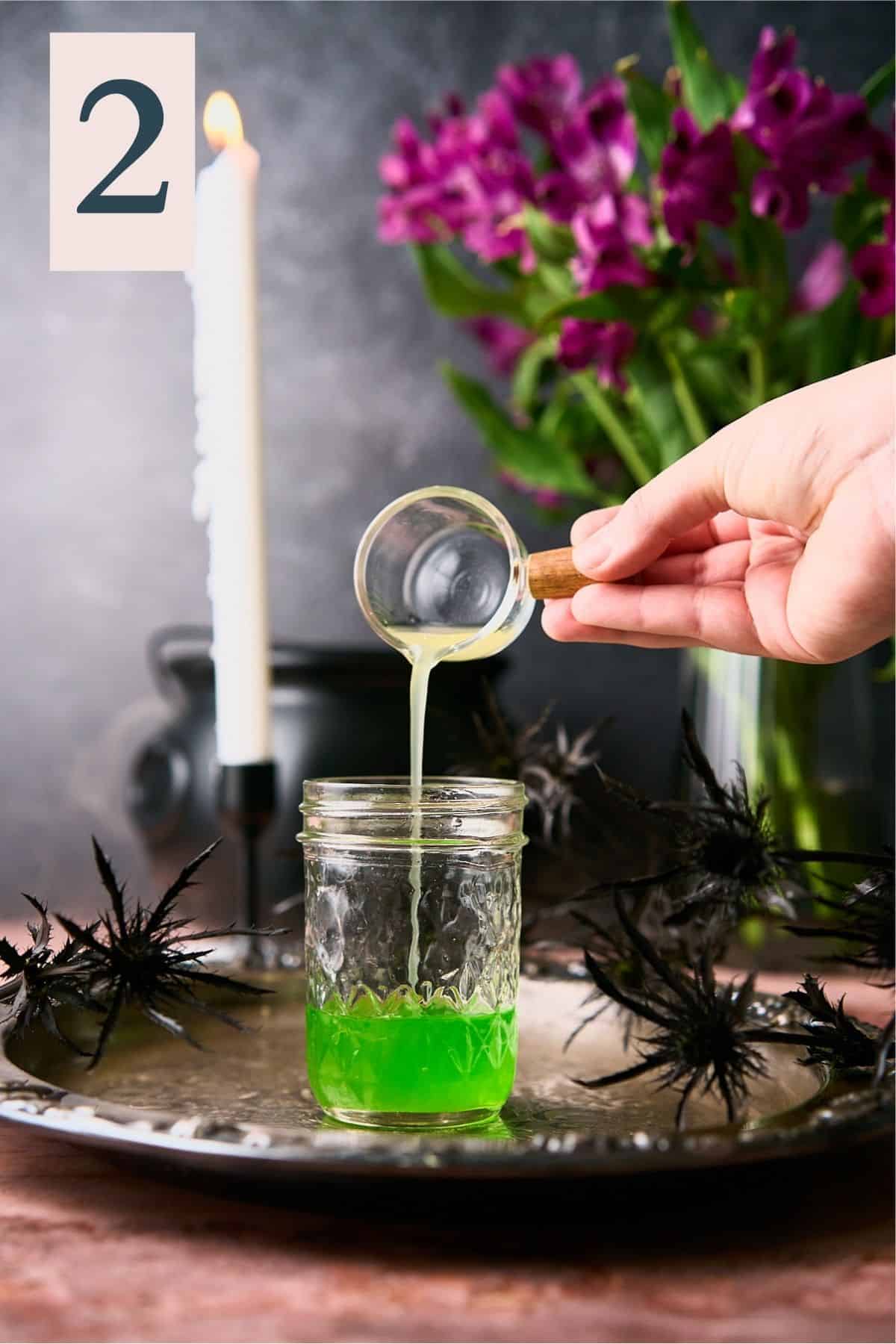 hand pouring pineapple juice into a jar with midori and a spooky backdrop. 