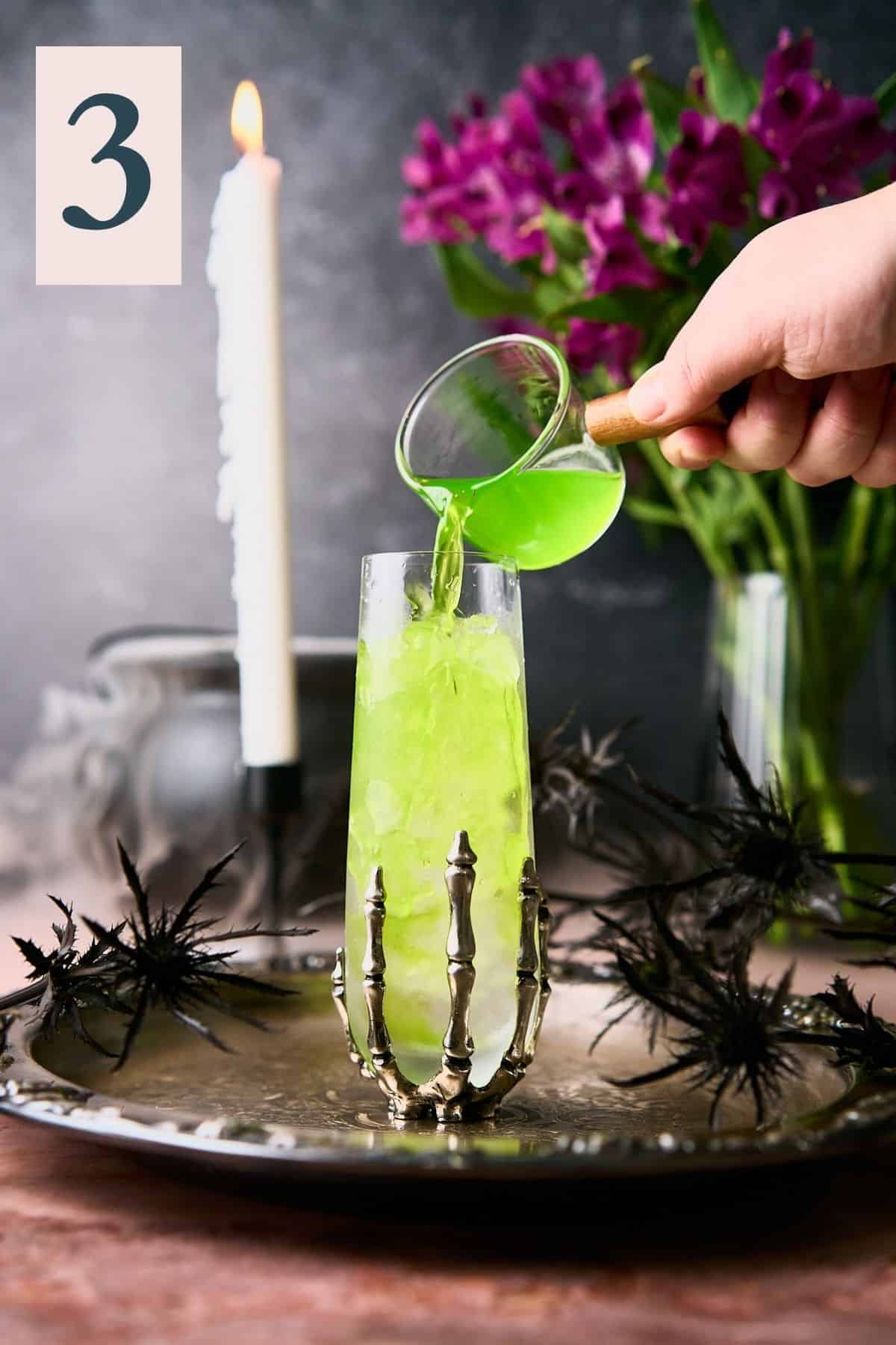 hand pouring green midori mixture into a glass with crushed ice. 