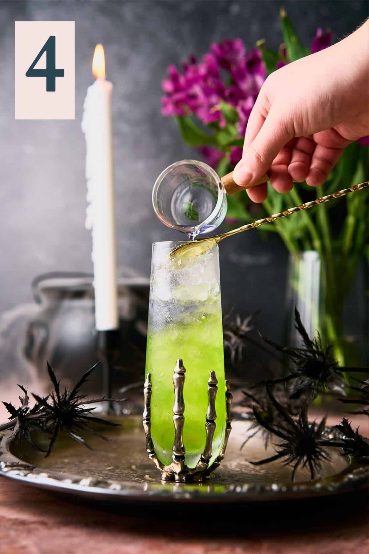 Hand pouring purple gin into a glass with green liquid. 