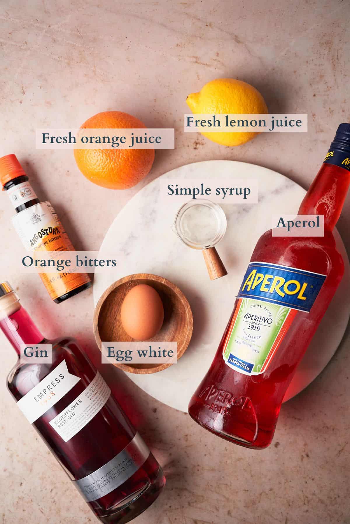 ingredients to make an aperol sour laid out on a table and labeled to denote each ingredient.