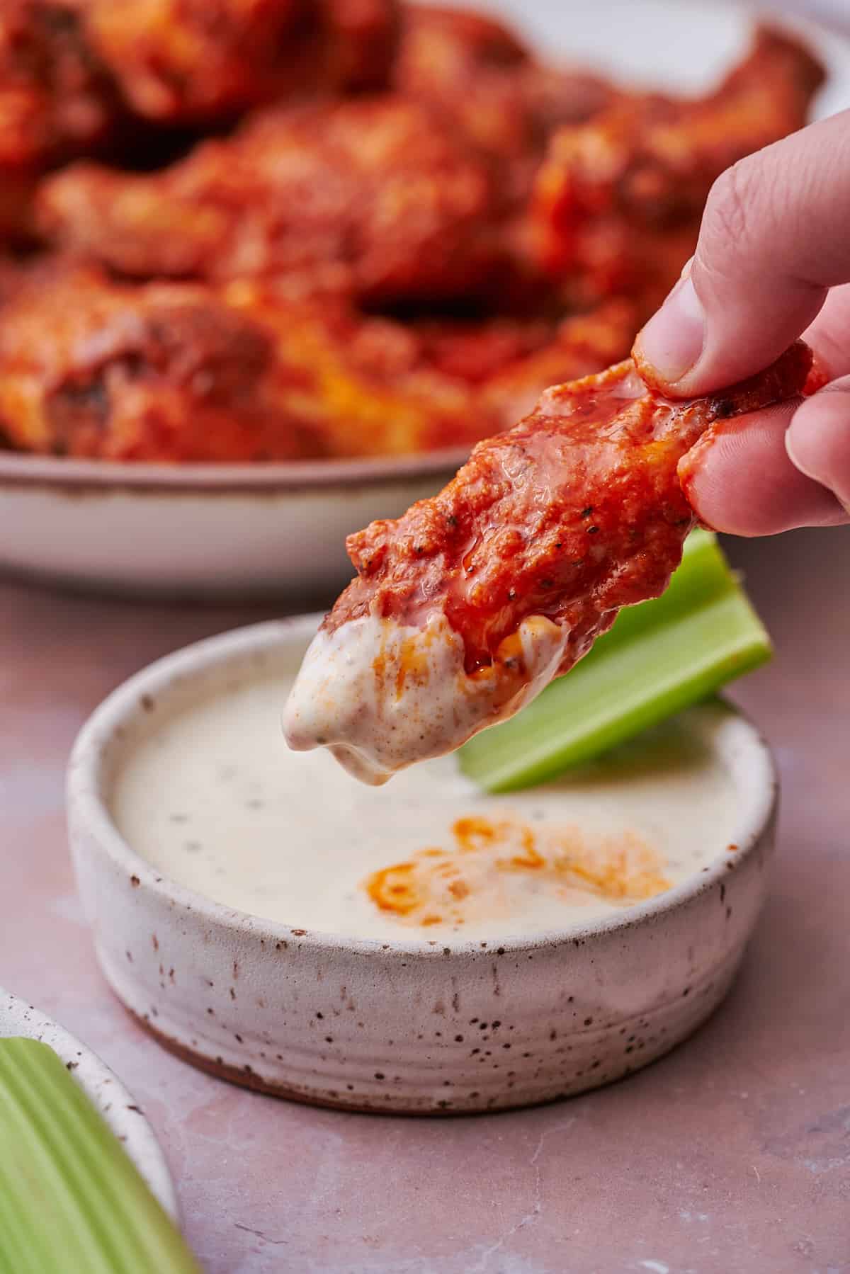 Buffalo wing being dipped in ranch, with celery stick on the side.