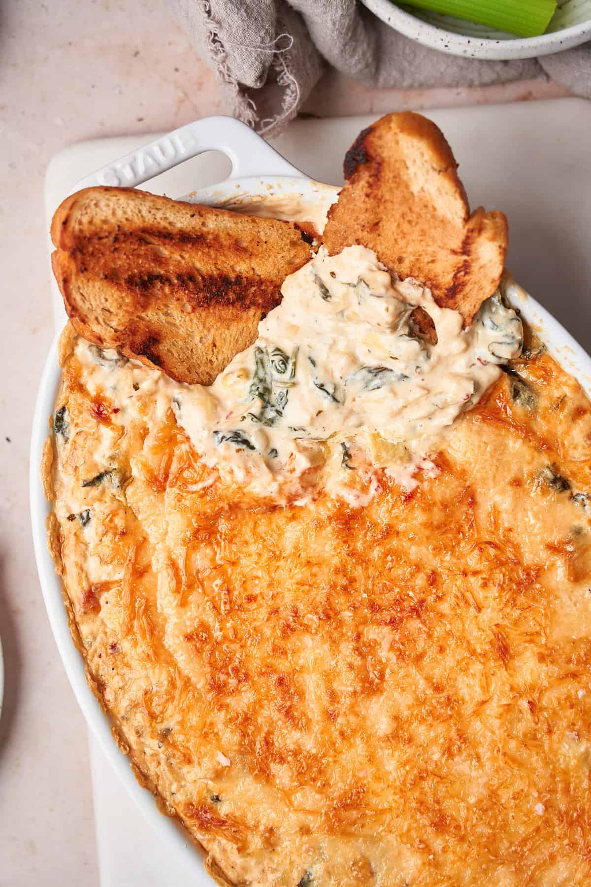 gooey and cheesy spinach artichoke dip in a white oval baking dish with grilled bread inside. 