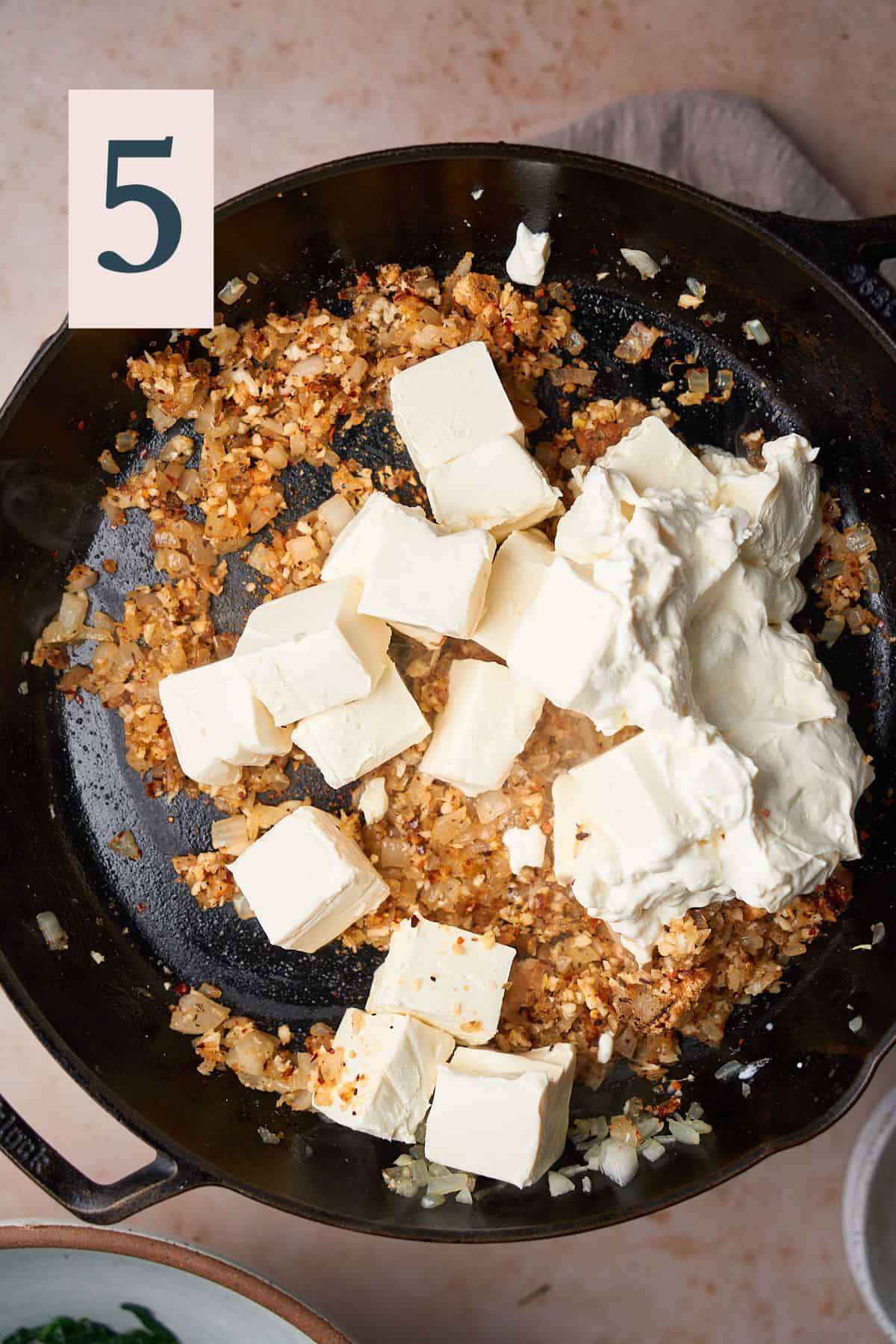 cubes of cream cheese and sour cream added to a skillet with cooked onion and garlic. 
