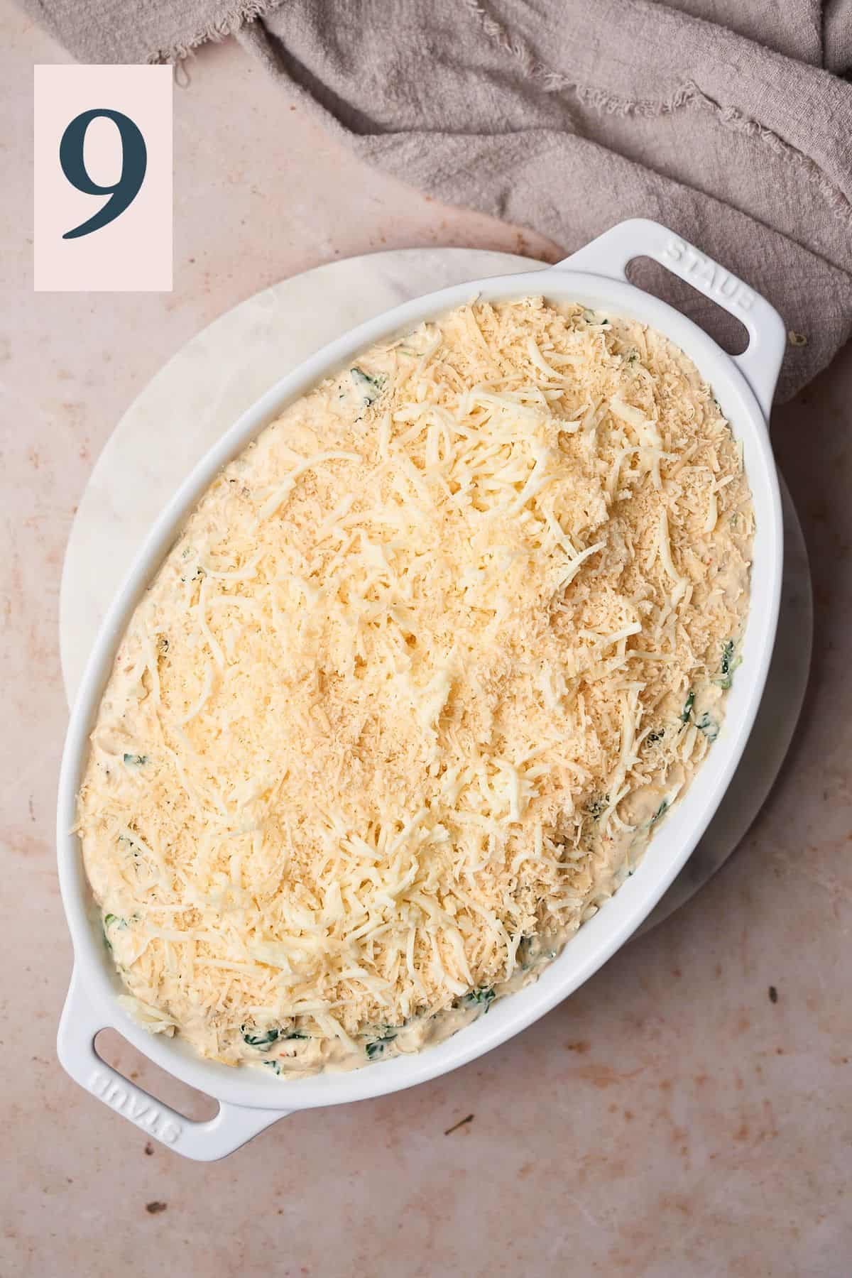 Spinach artichoke dip transferred to an oval baking dish topped with mozzarella and parmesan cheese. 