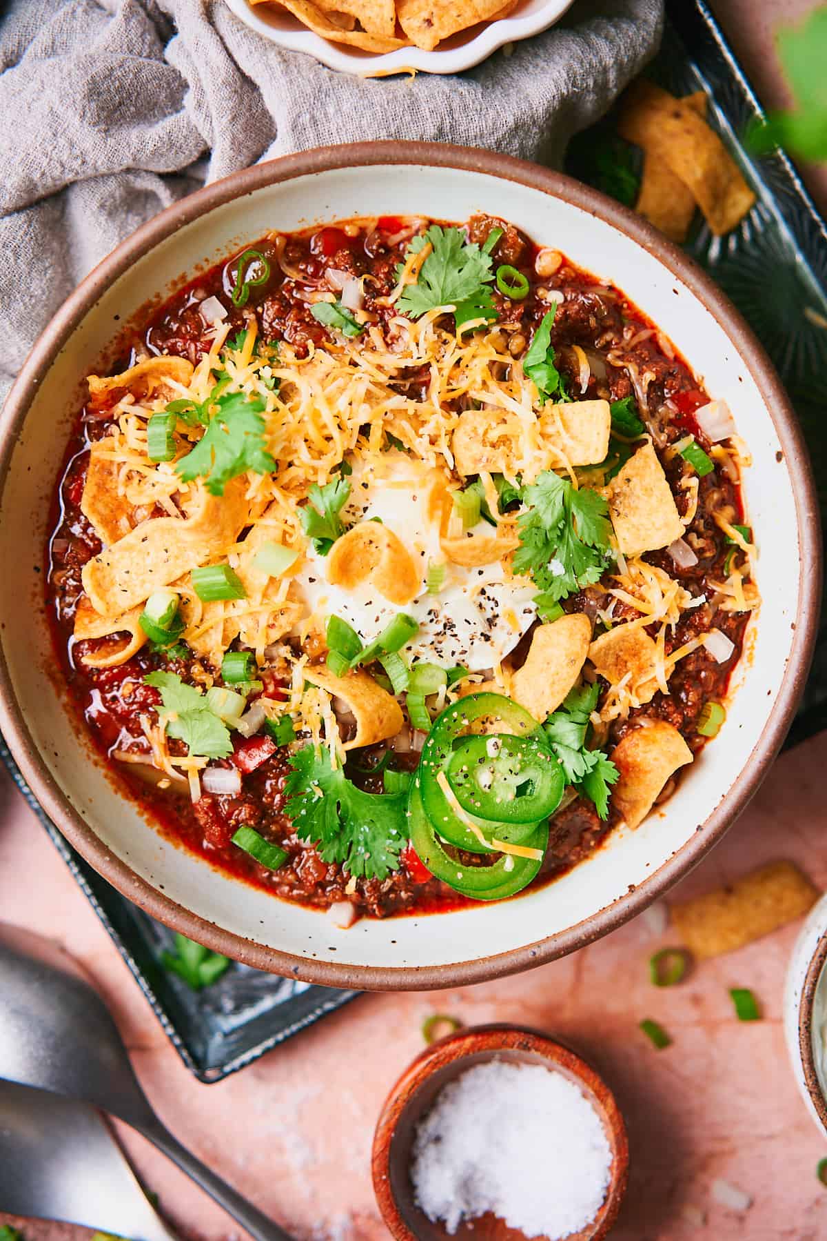 large bowl of chili topped with sour cream, cheese, cilantro, jalapenos, green onions, raw onions and fritos. 