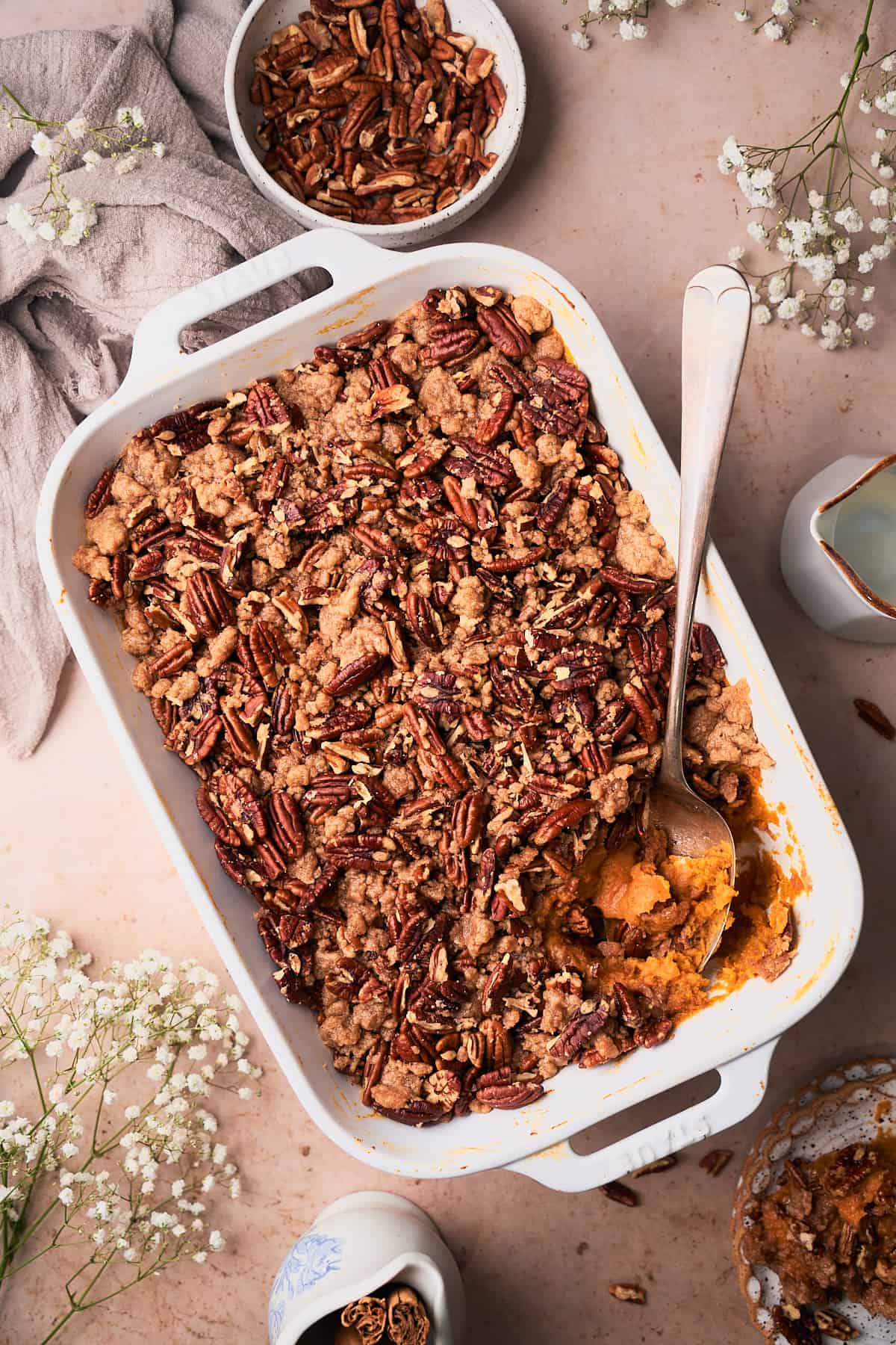 Rectangular casserole with sweet potato casserole with a pecan topping, with baby's breath and pecans surrounding on the scene. 