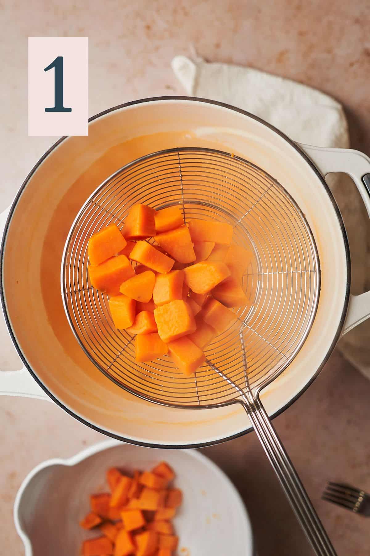 boiled sweet potatoes fin a skimmer coming out of water from a pot. 