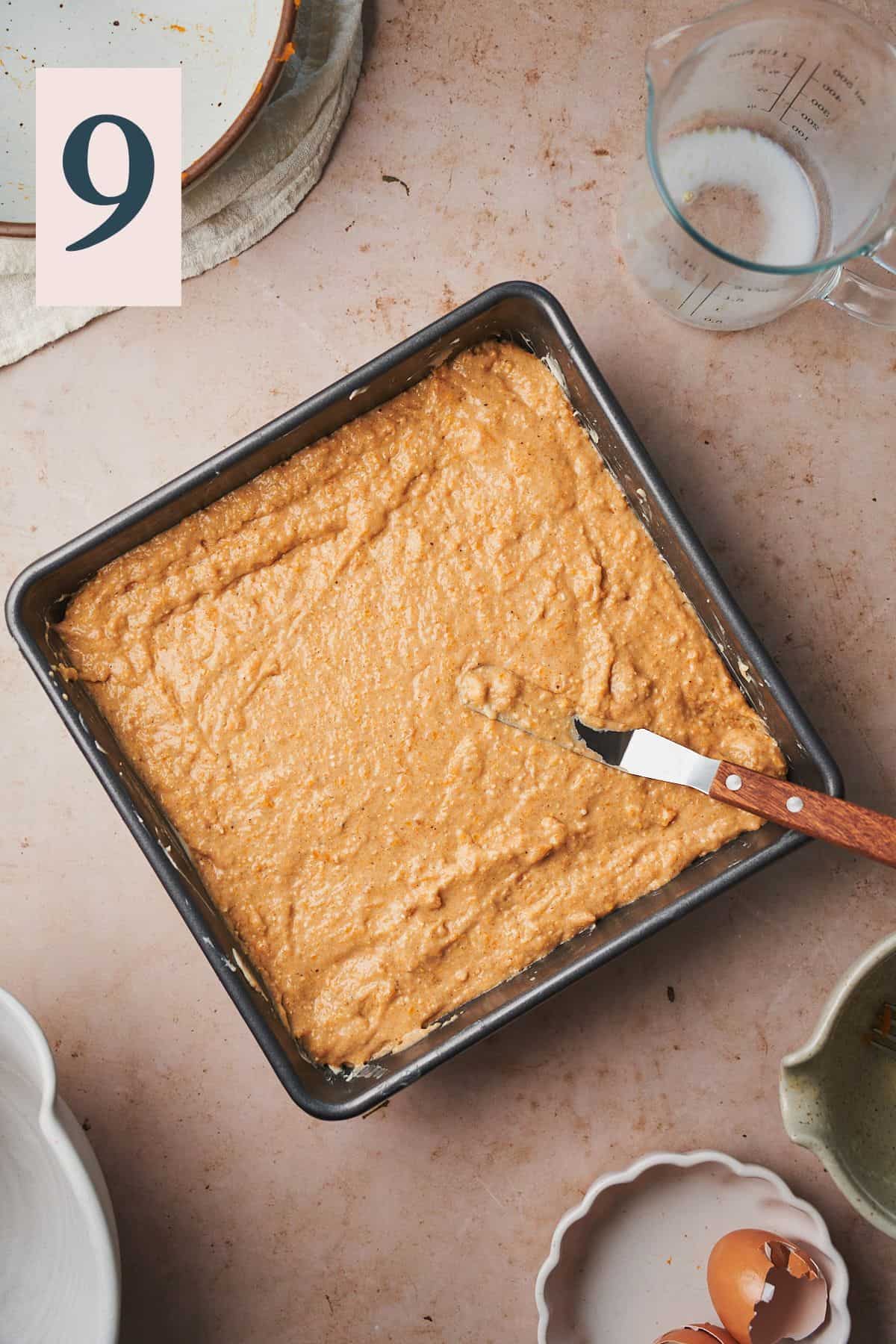 cornbread mixture spread in a square baking pan with an offset spatula. 