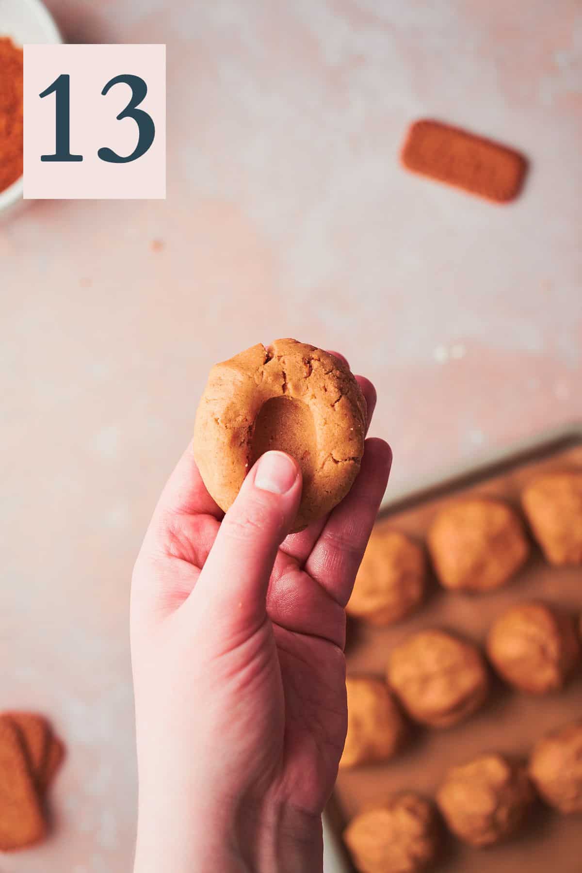 hand pressing a thumb sized hole into the center of a ball of cookie dough. 