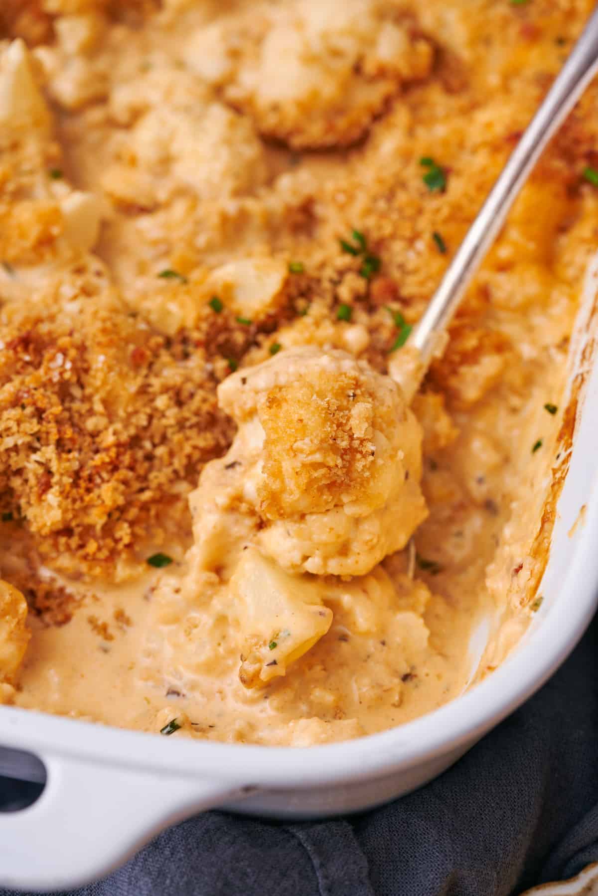 Spoonful of cheesy baked cauliflower on a spoon with a breadcrumb topping. 