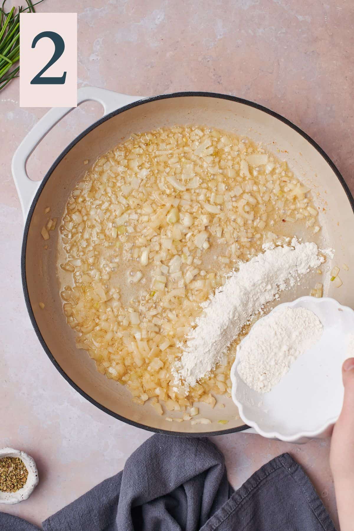 onions cooking in butter in a skillet, with a hand adding flour to the skillet. 