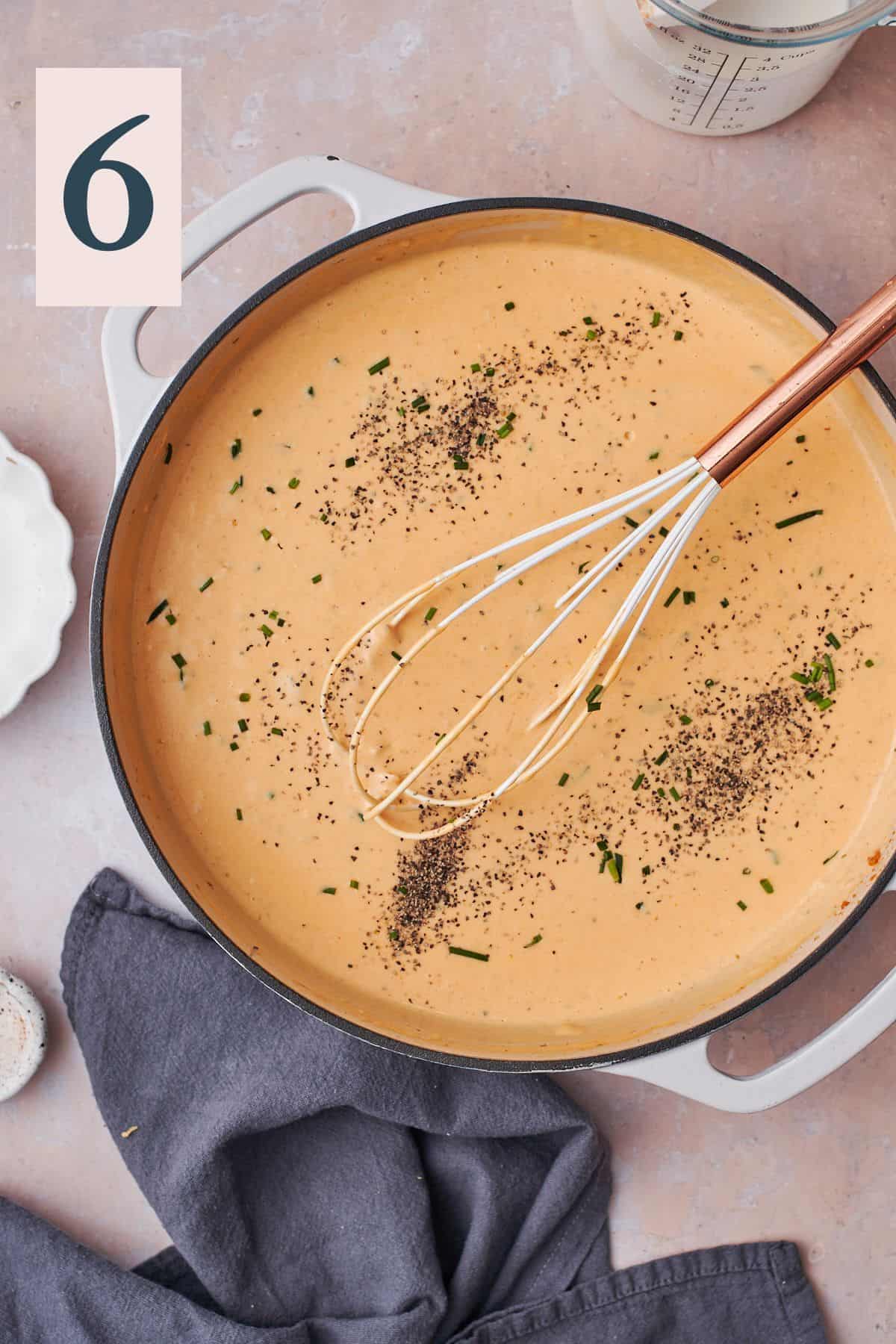 cheesy sauce in a skillet with a whisk with pepper added to the sauce.