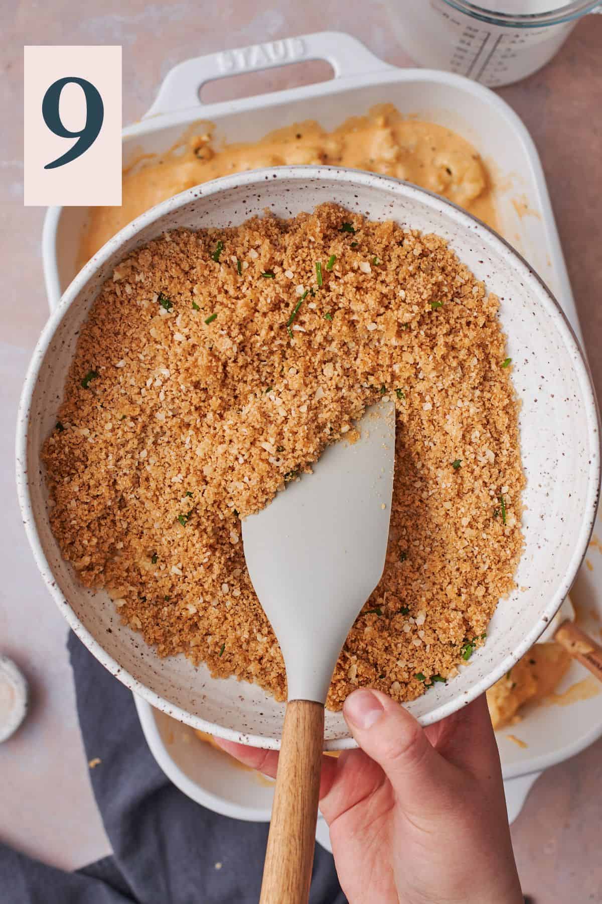 hand using a rubber spatula to combine breadcrumbs with salt, parmesan cheese, melted butter, and herbs. 