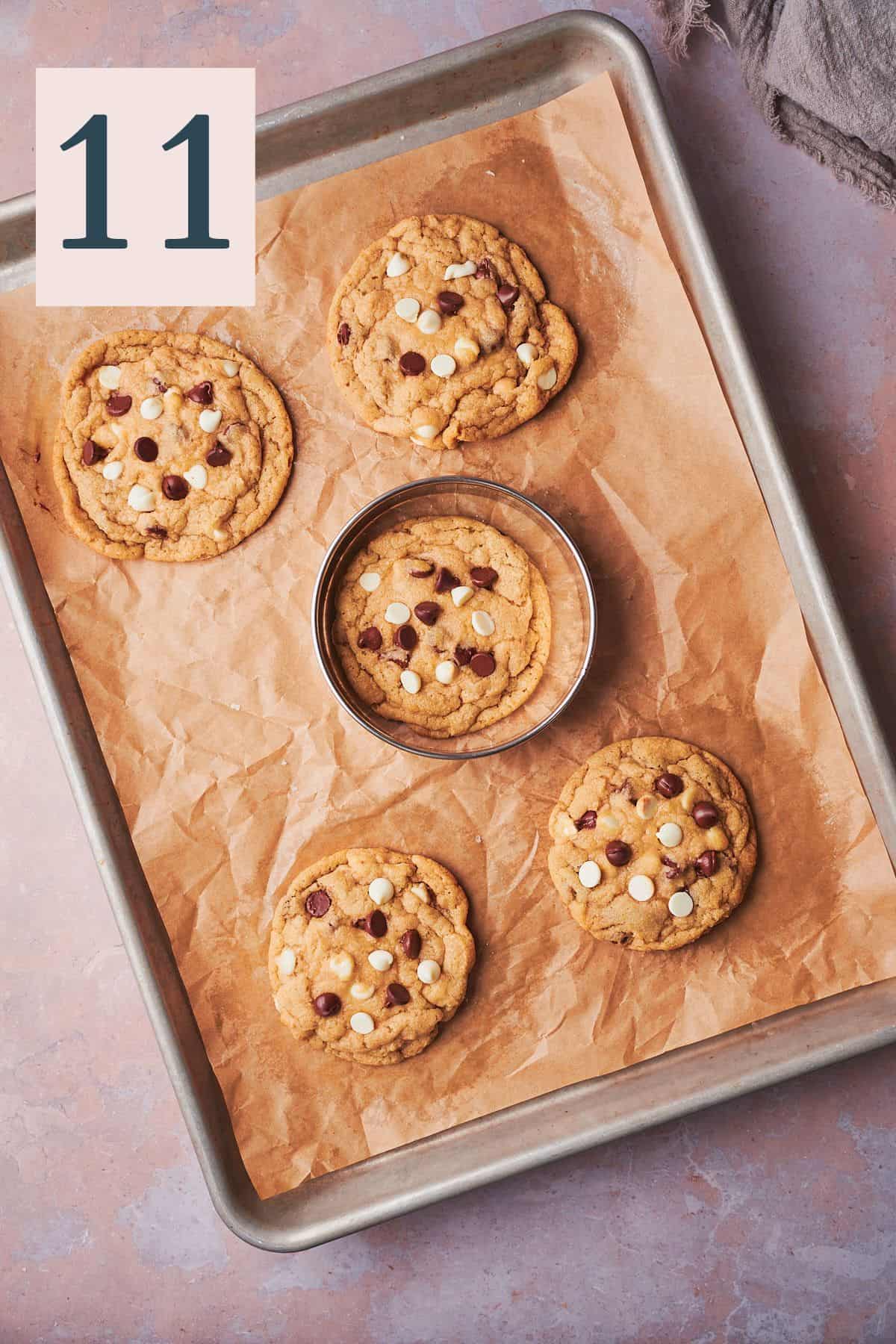 baked cookies on a baking sheet with a biscuit cutter surrounding them to scoot them into a round shape. 