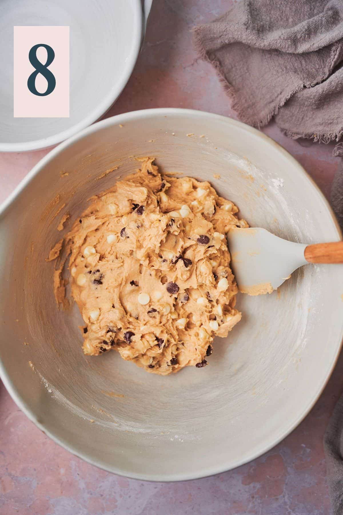 cookie dough with chocolate chips mixed in in a large bowl, with a rubber spatula in the bowl. 