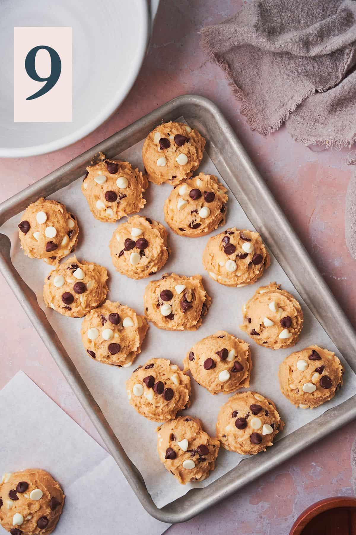 balls of cookie dough on a small baking sheet topped with more white and semi-sweet chocolate chips. 