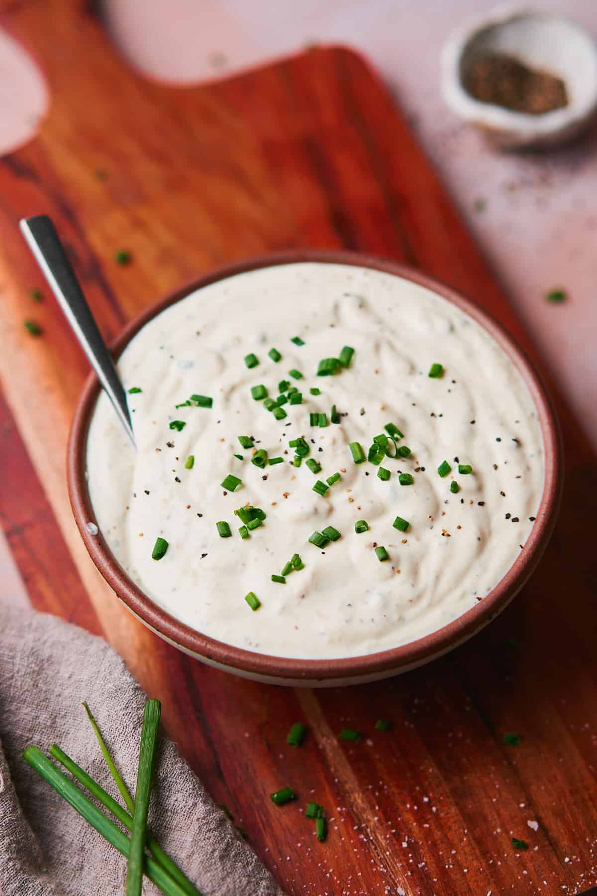 close up shot of creamy horseradish sauce on a wooden board and topped with fresh chives. 