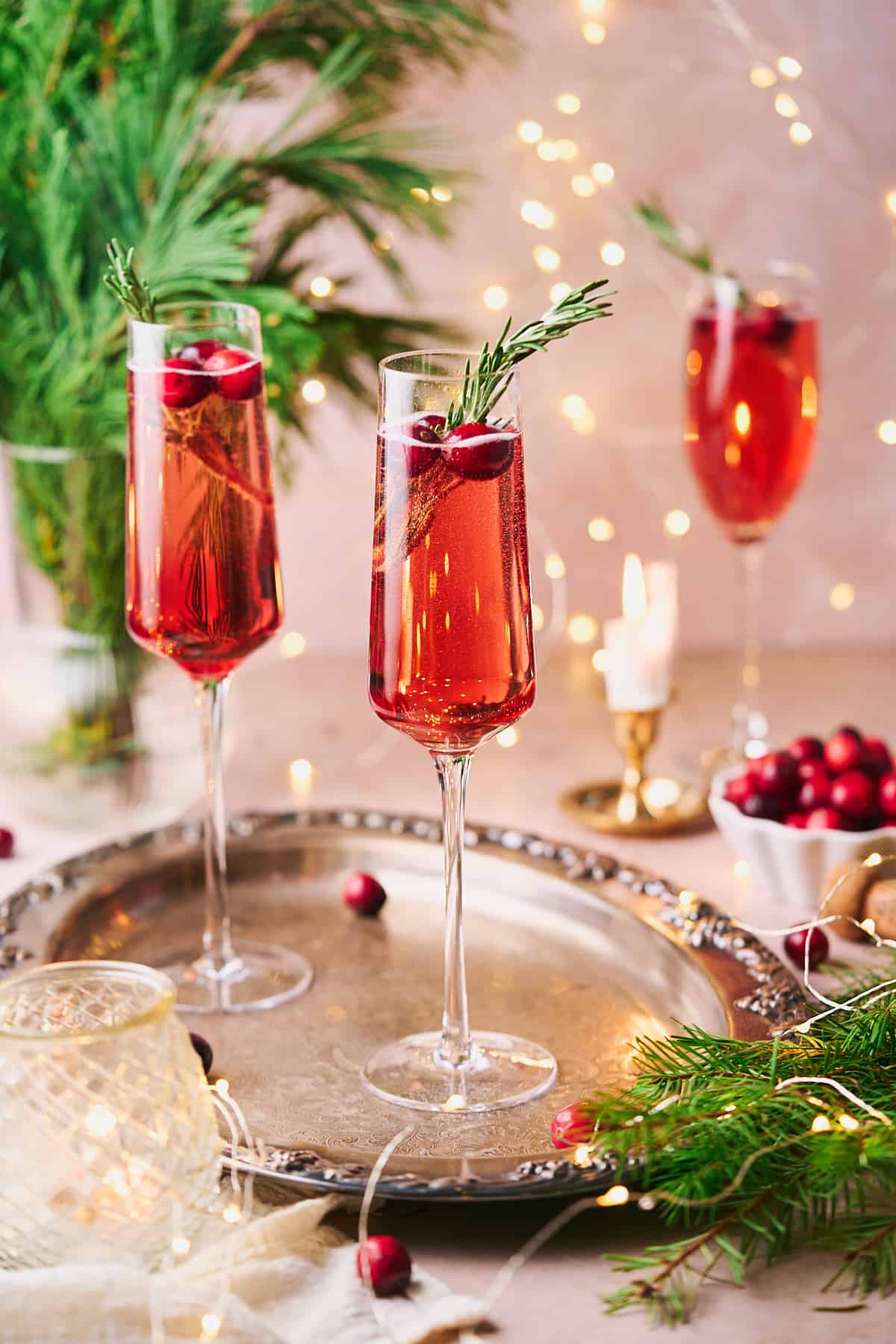 stunning bright red poinsettia cocktails with twinkle lights in the background, with fresh cranberries, and green garland. 