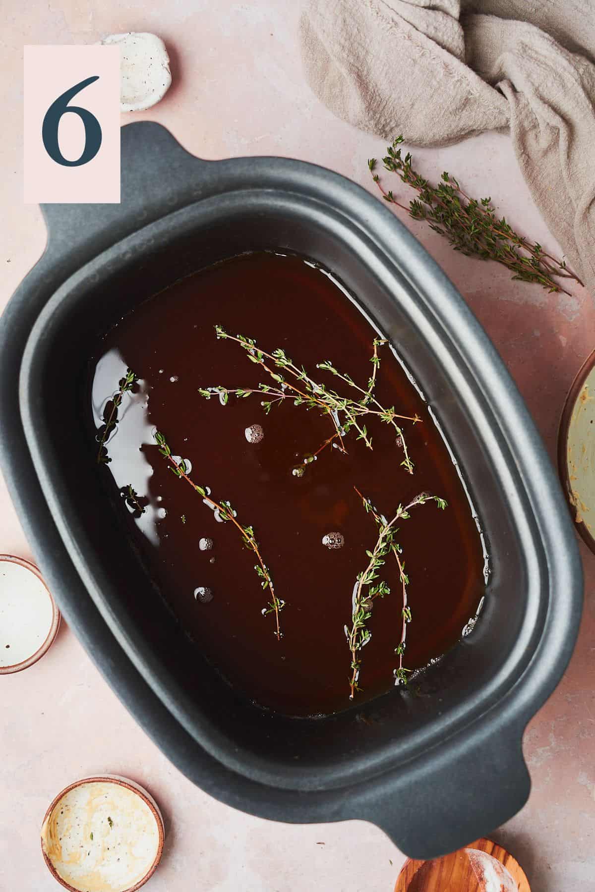 beef stock and thyme sprigs in the bottom of a slow cooker. 