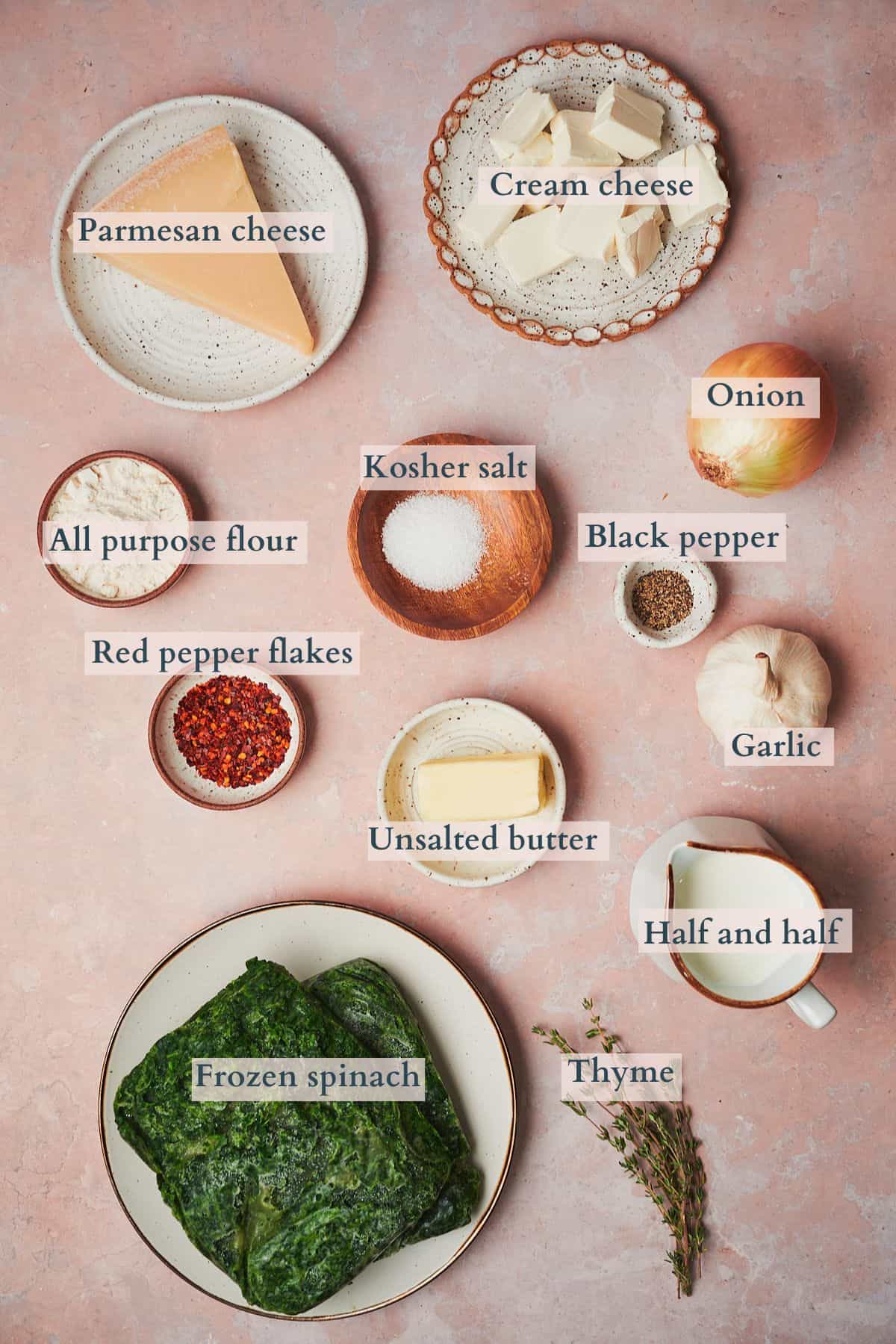 Ingredients to make creamed spinach laid out in small bowls and on a table, labeled to denote each ingredient. 