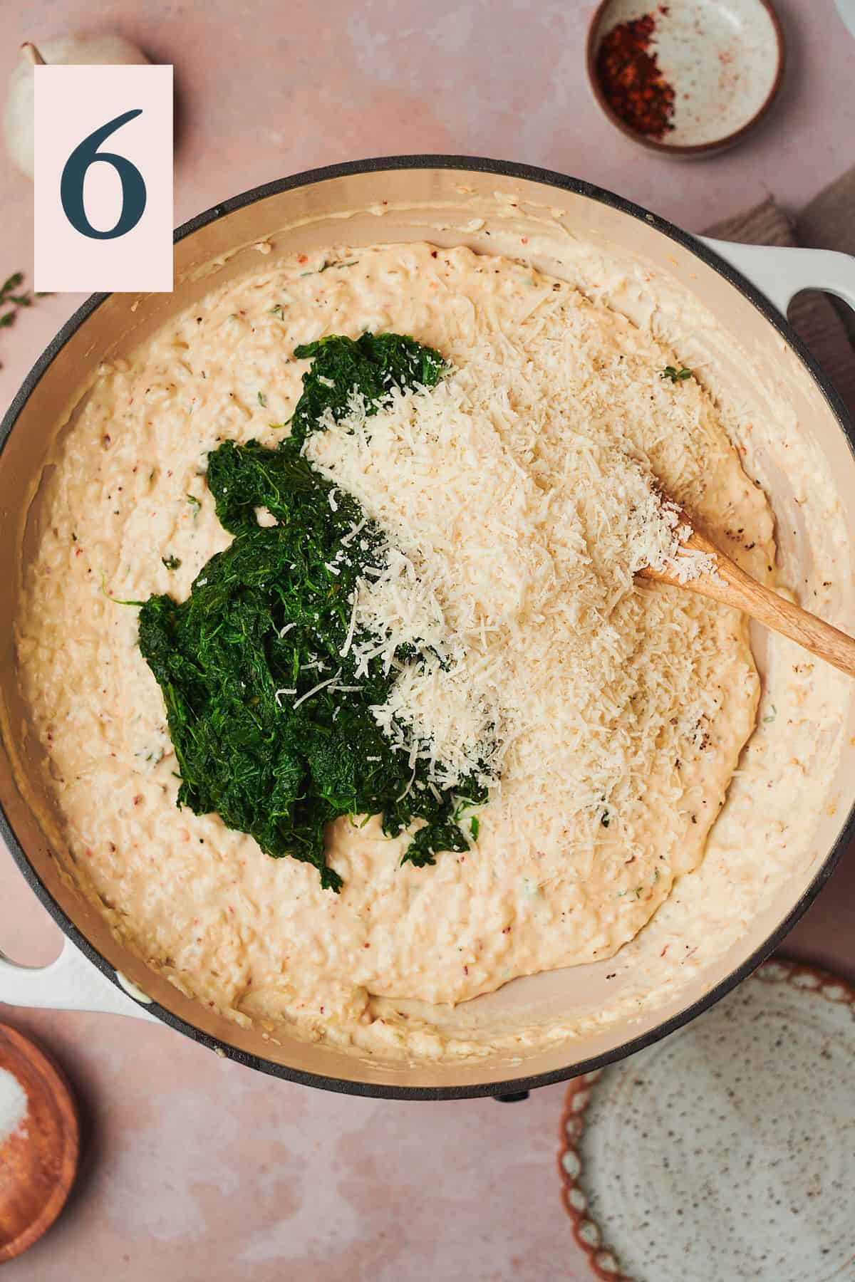 spinach and some parmesan cheese added to a skillet with a creamy sauce in it. 
