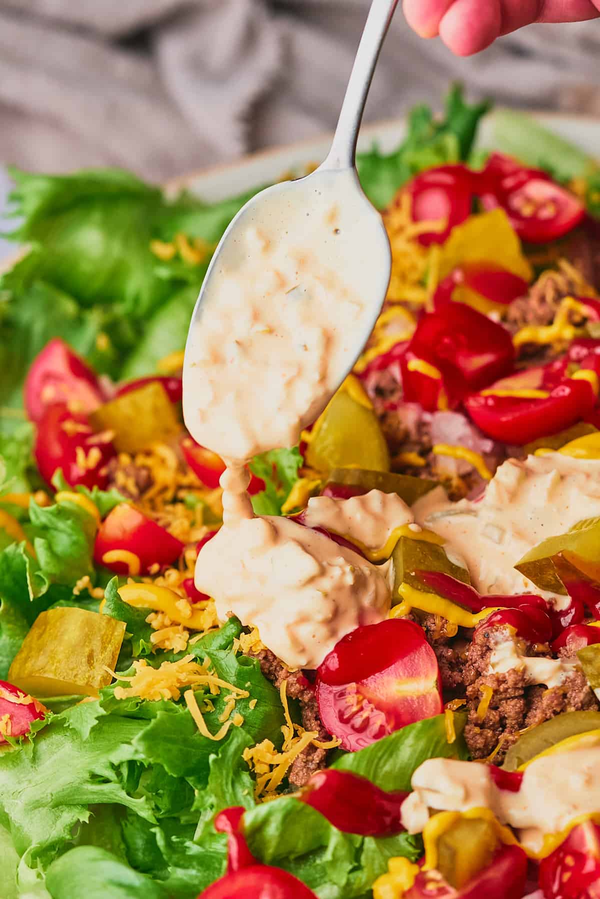 Spoonful of big mac dressing being drizzled onto a cheeseburger salad. 