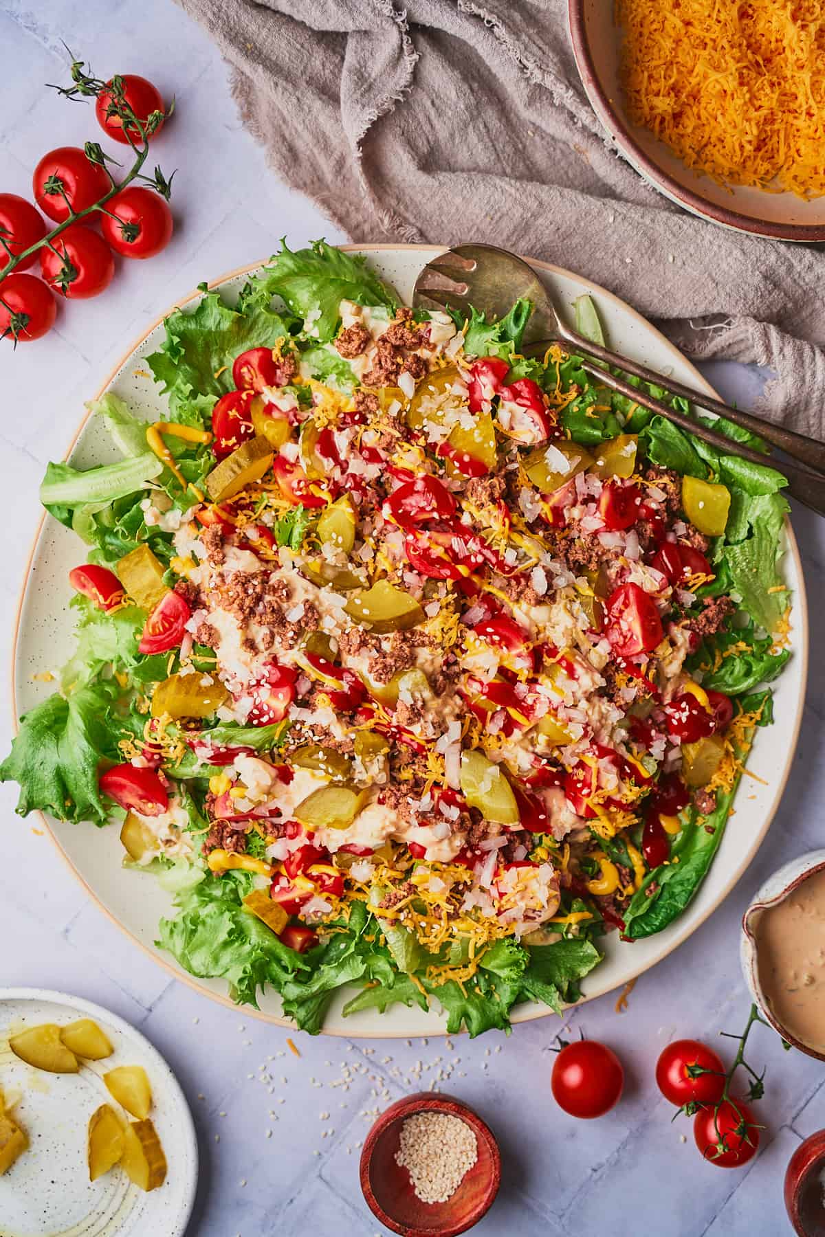 Large big mac burger salad on a round plate, surrounded by tomatoes and other ingredients to make the salad. 