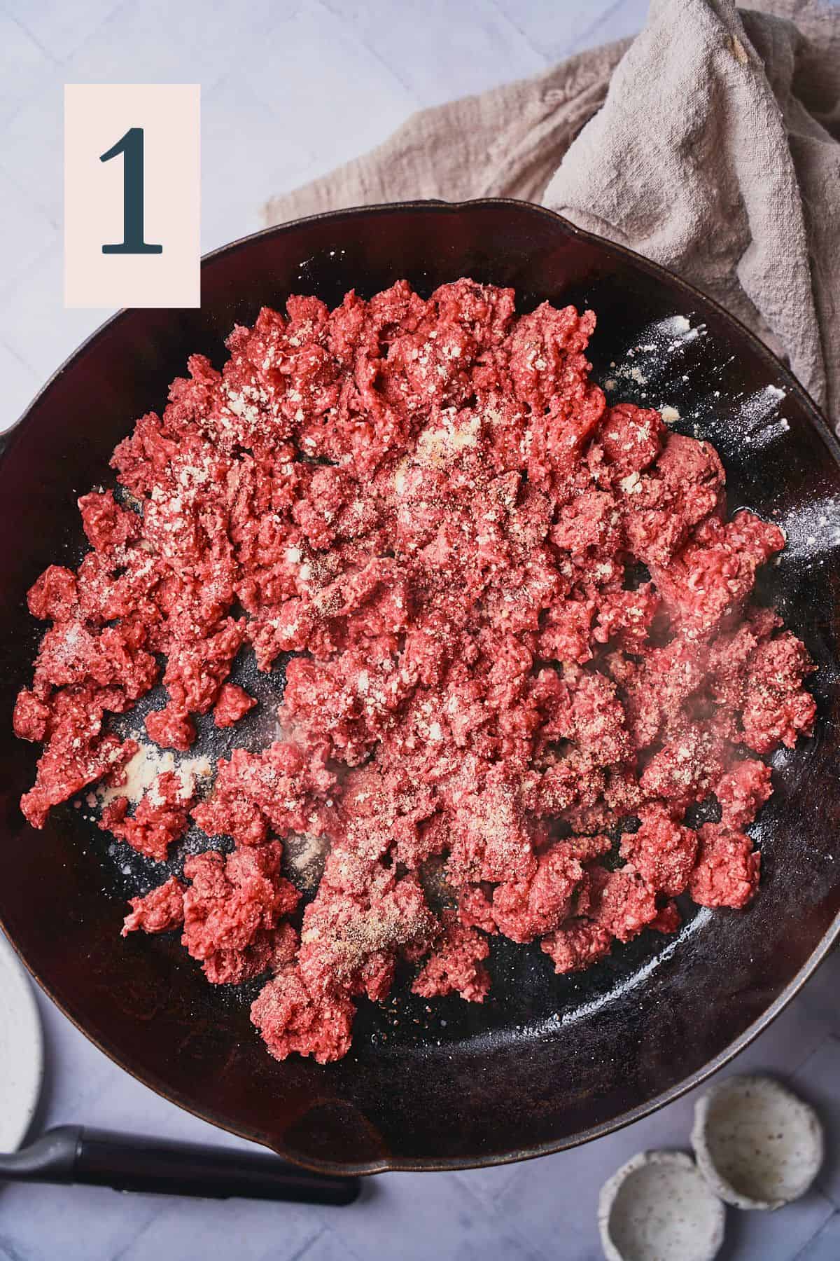 raw ground beef in a skillet seasoned with garlic and onion powder. 