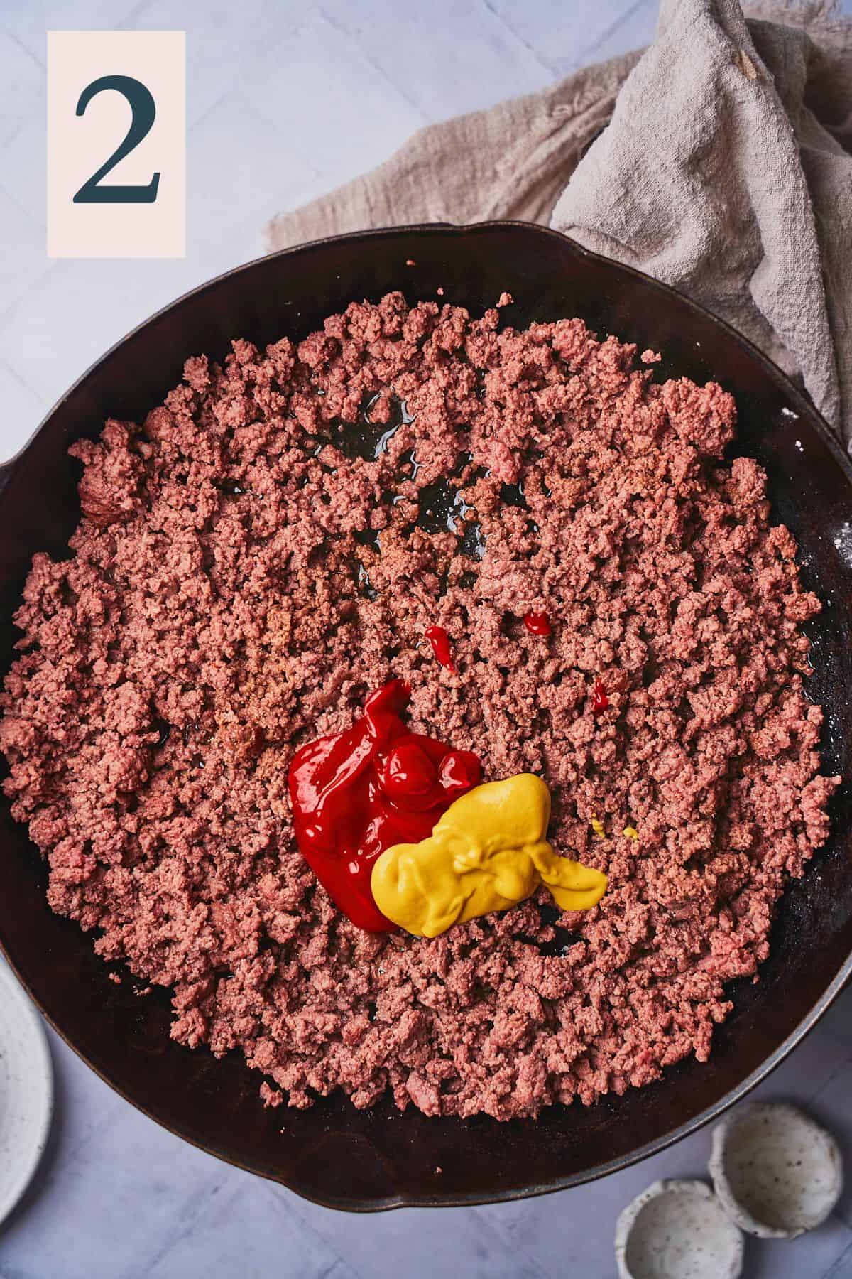 cooked ground beef in a skillet seasoned with ketchup and mustard.