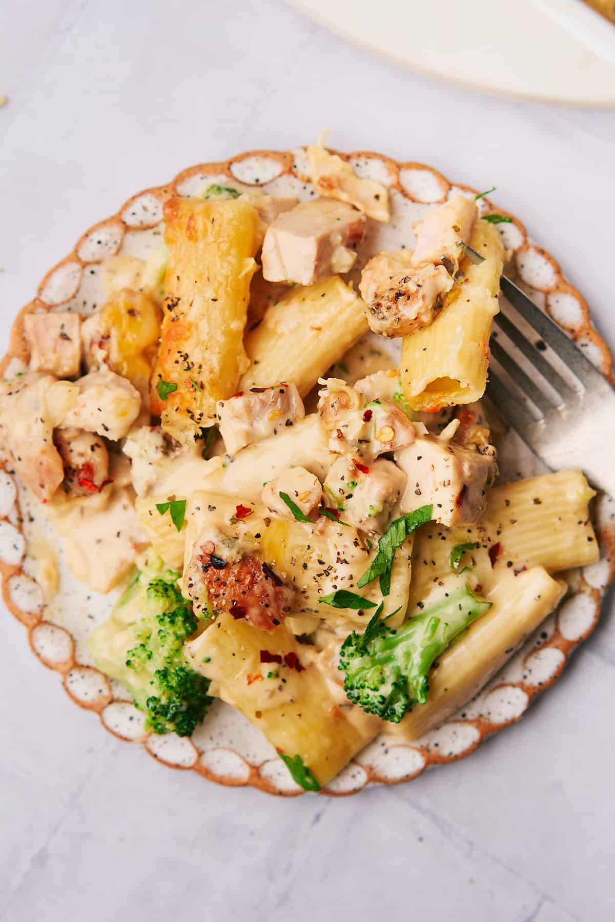plate of chicken and broccoli pasta with rigatoni, topped with parsley and pepper. 
