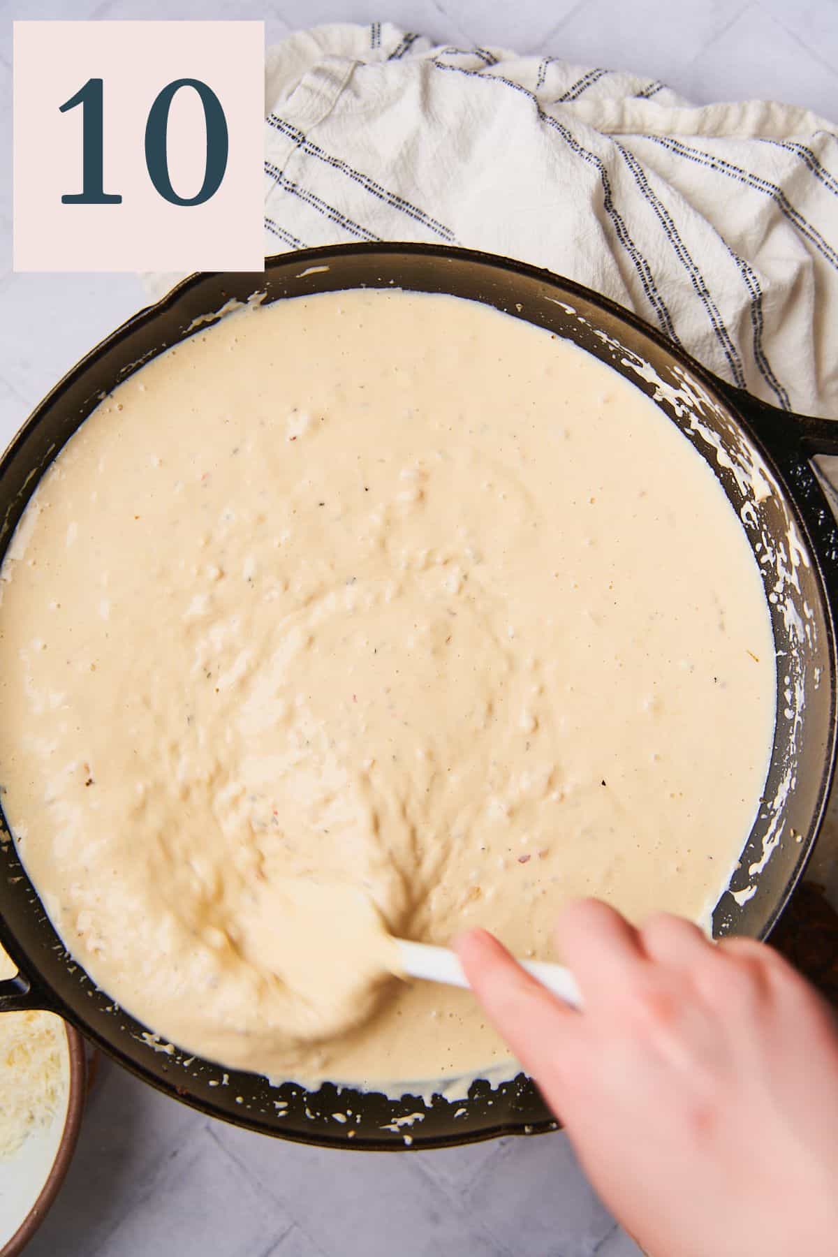 rich and creamy cheese sauce in a skillet with a hand stirring it with a rubber spatula. 