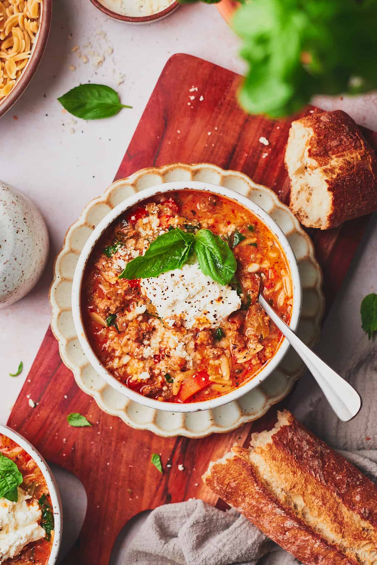 Bowl of Italian sausage soup on a ruffled plate with fresh bread surrounding it, ricotta on top, and basil. 