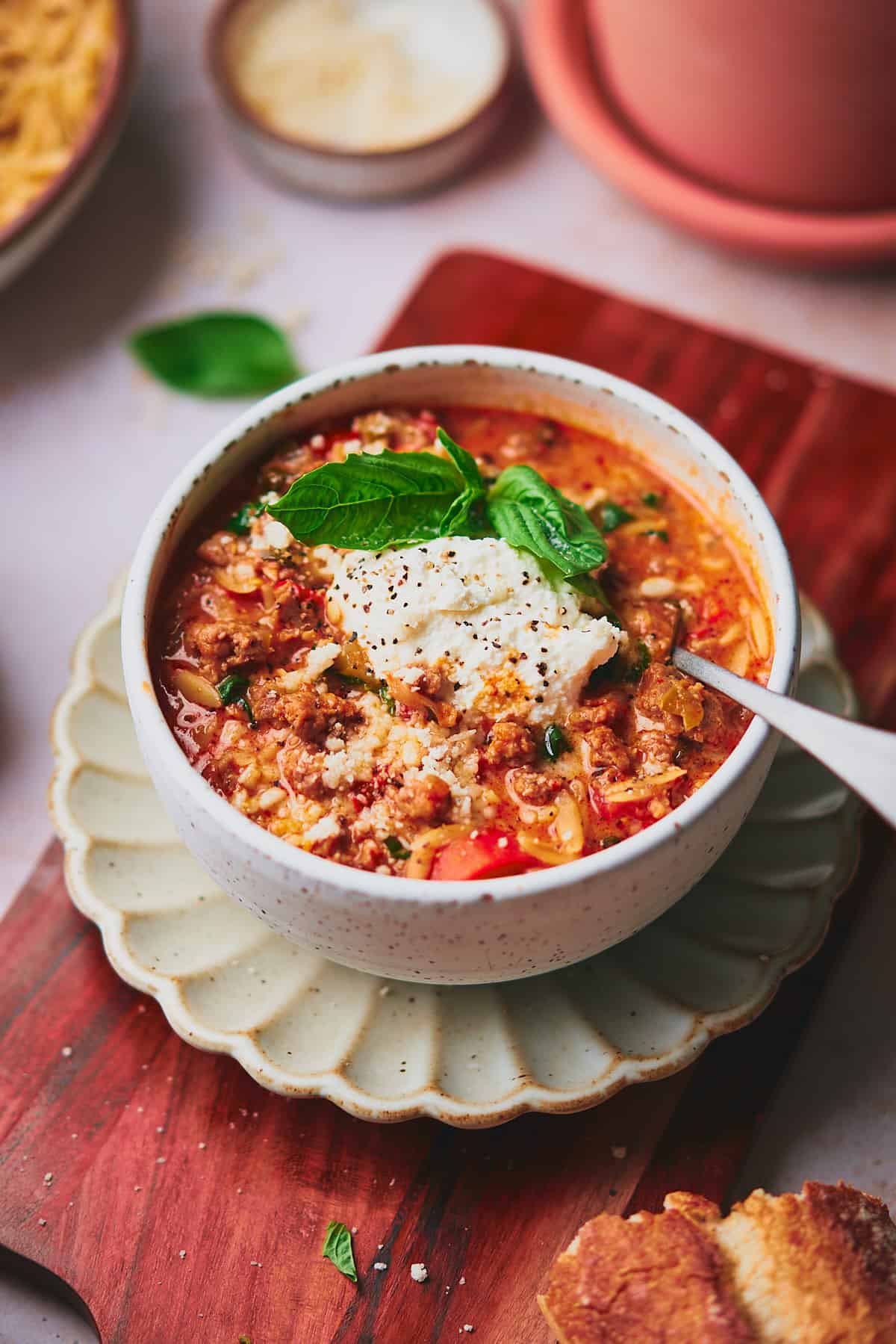 Italian sausage soup with orzo in a bowl topped with basil, ricotta, and parmesan cheese. 
