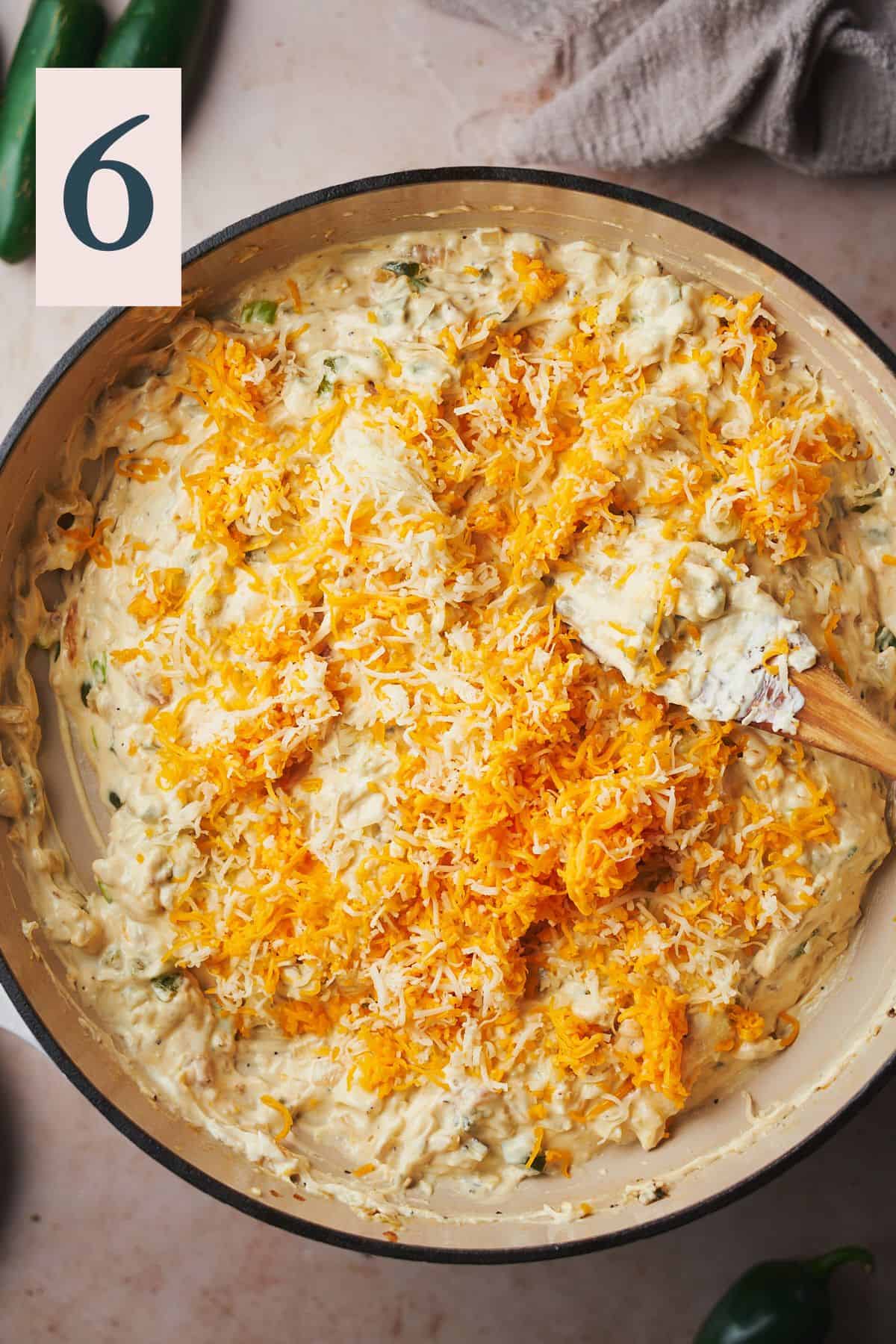 Shredded cheese added to a cream cheese mixture in a skillet.