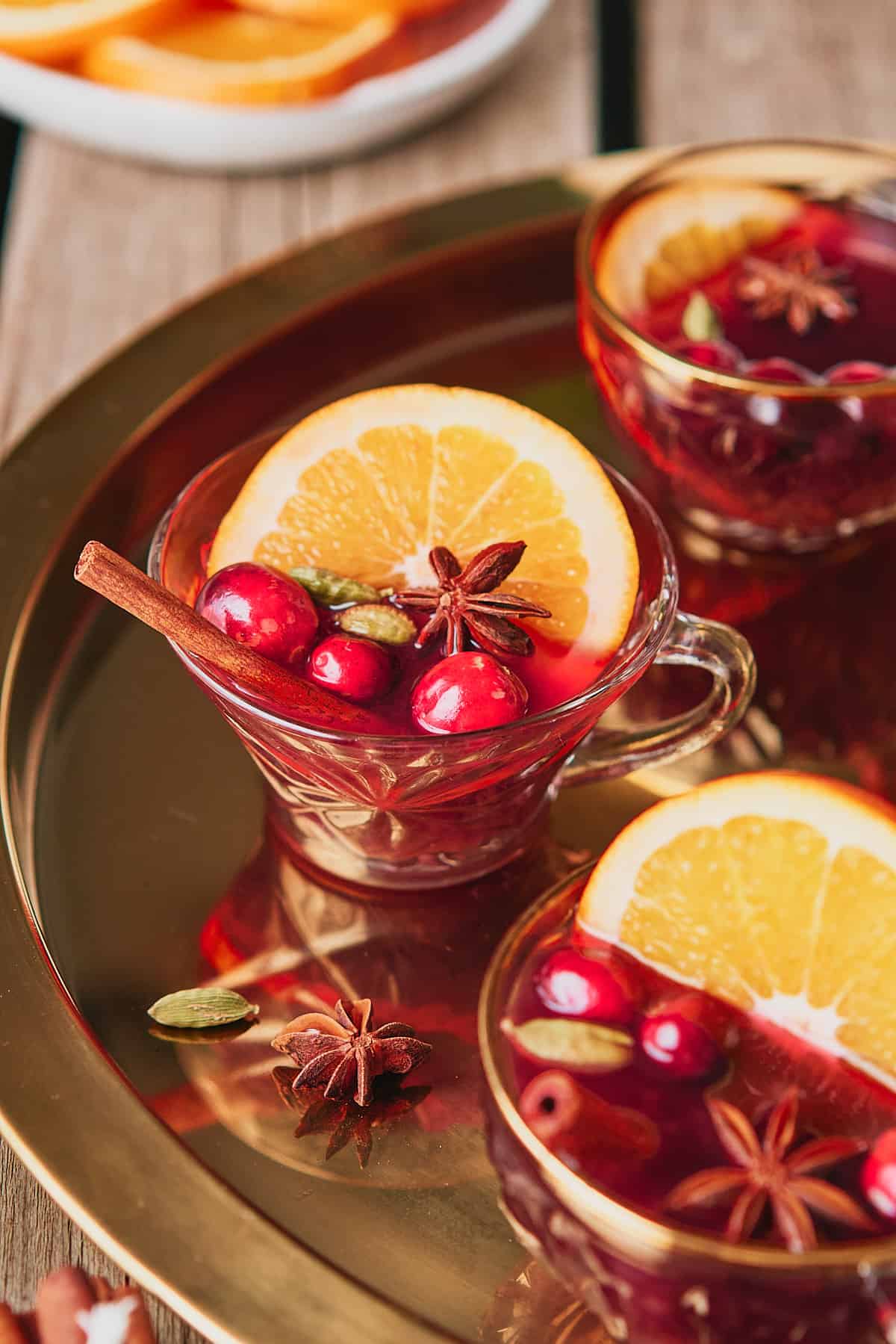 Stunning mulled gin and wine in a glass tea cup on a gold platter, served with an orange slice, star anise, cranberries and a cinnamon stick. 