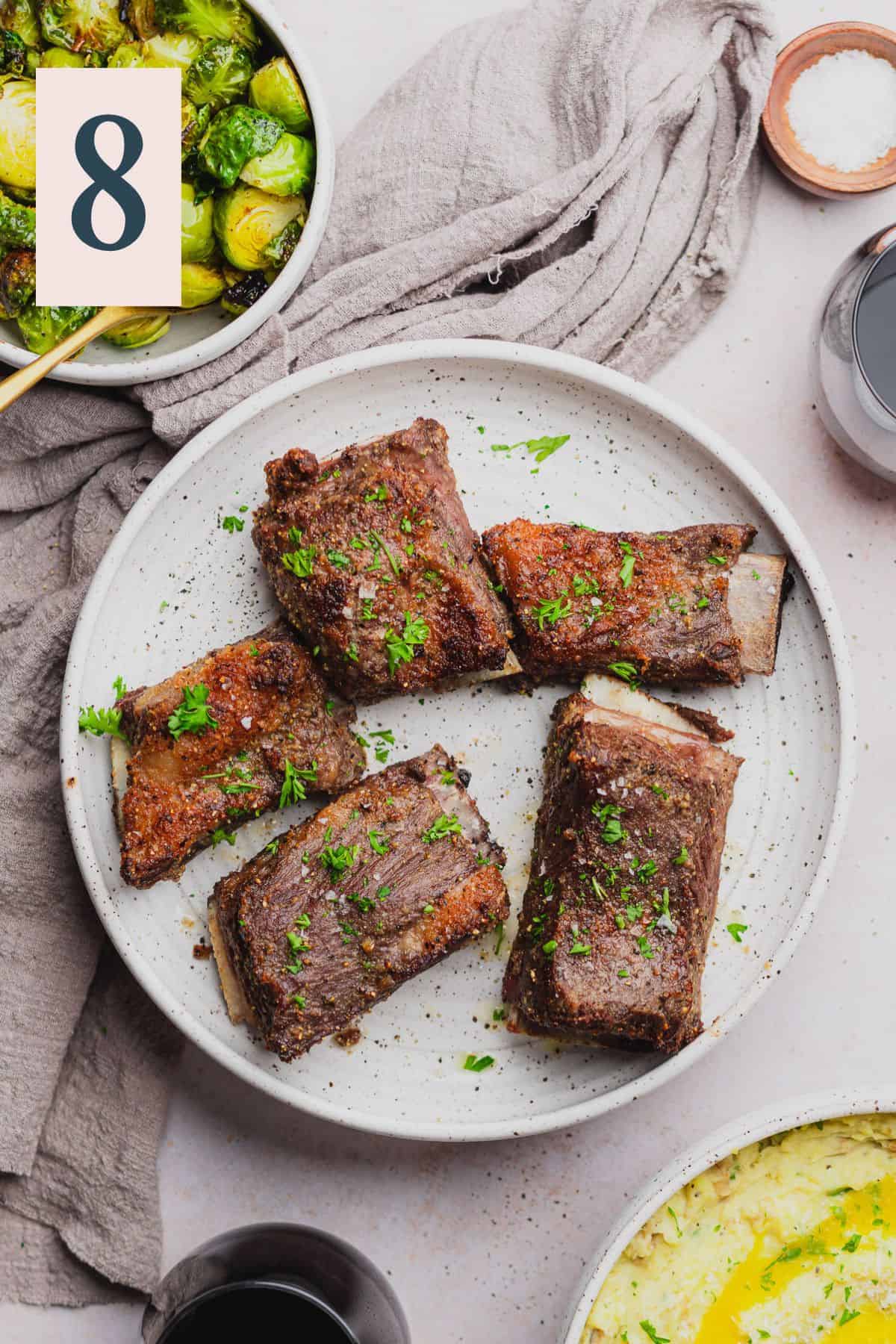air fryer short ribs on a plate with red wine, brussel sprouts, and mashed potatoes nearby