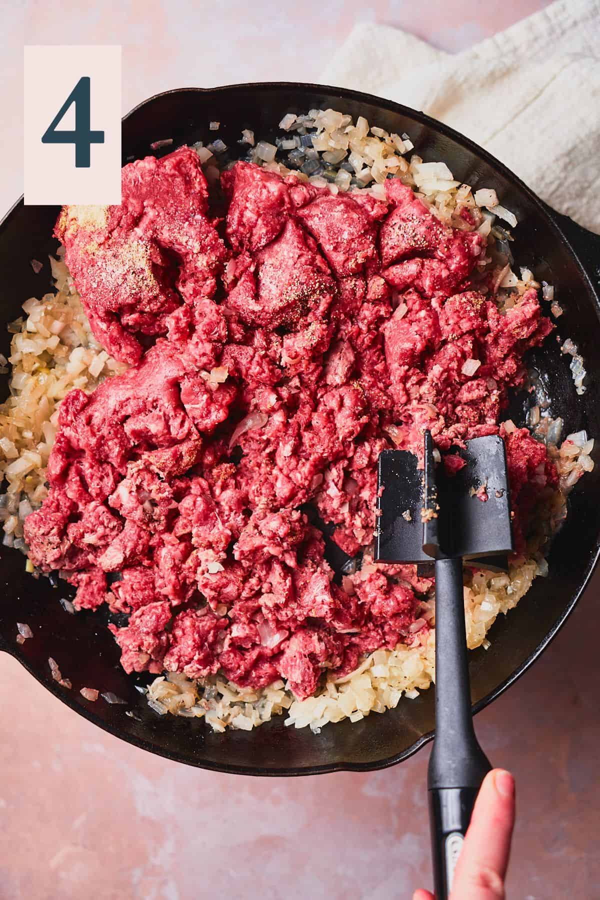 Raw ground beef in a cast iron skillet with onions. 