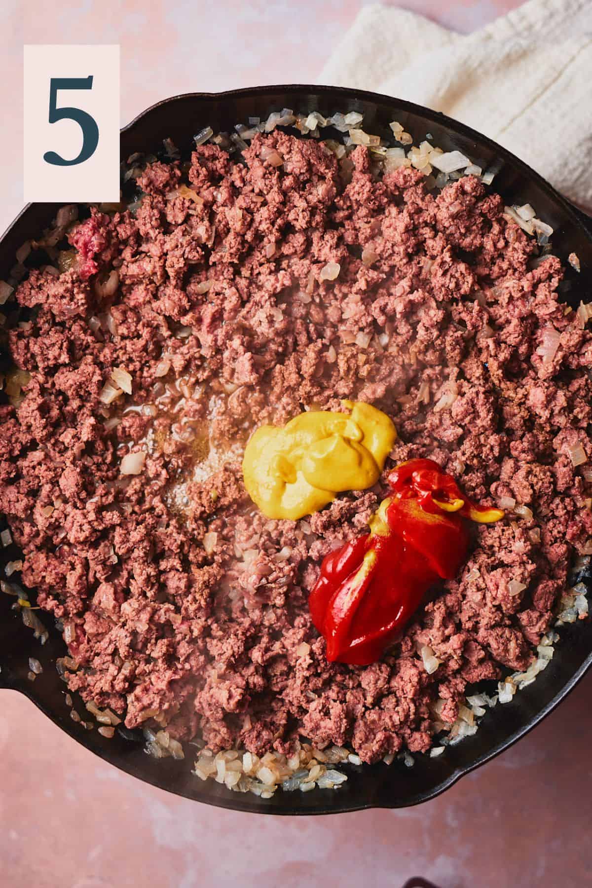 Cooked ground beef in a skillet with ketchup and mustard added. 